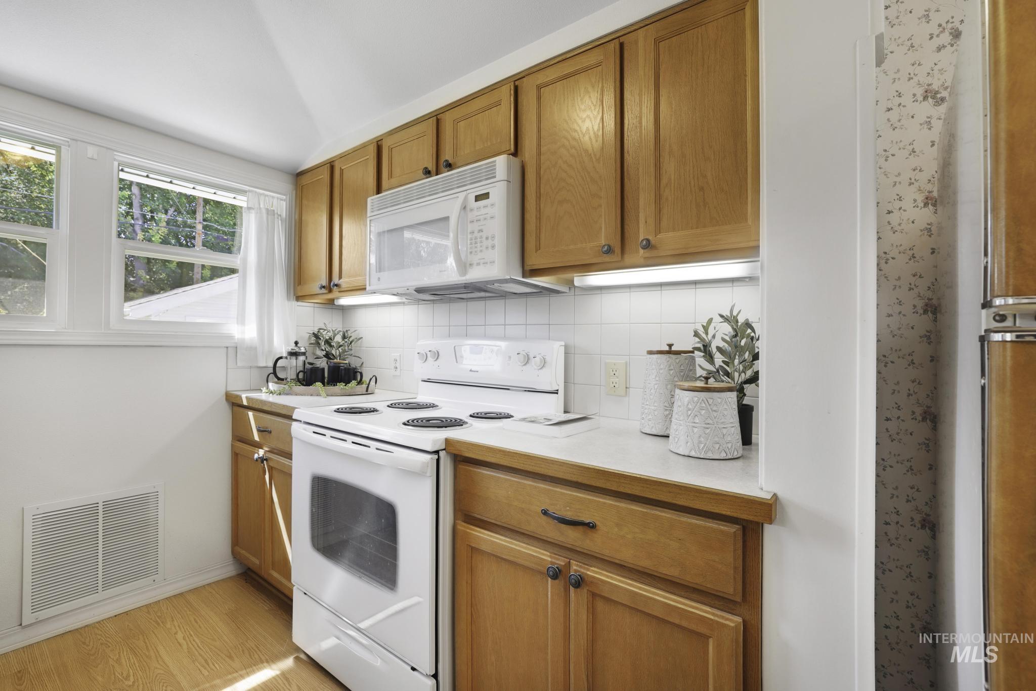 Kitchen featuring white appliances, decorative backsplash, light countertops, brown cabinets, and light wood-style flooring