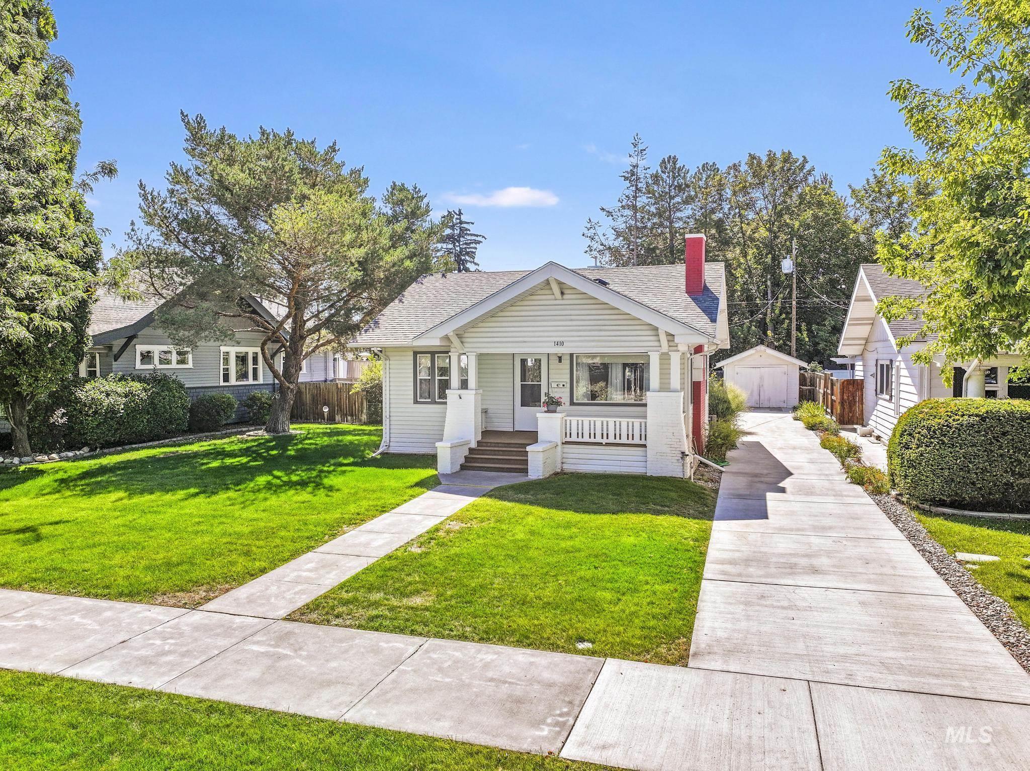 Bungalow-style home with an outbuilding, a chimney, a shingled roof, and a porch
