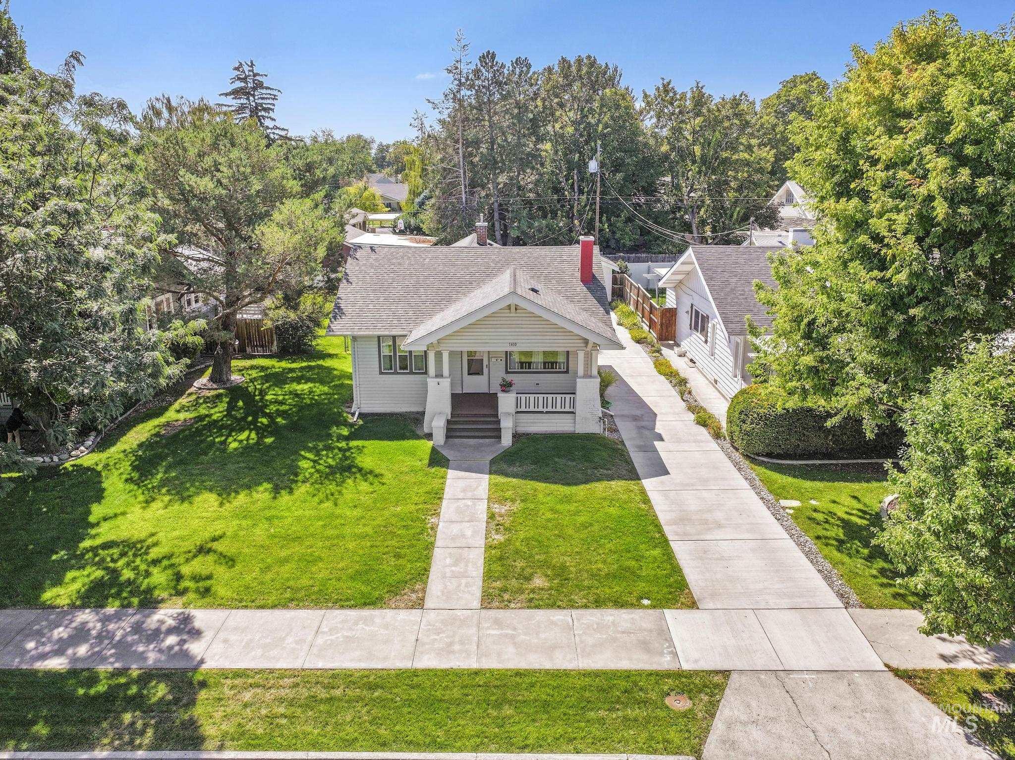 Bungalow featuring a porch, a front yard, a shingled roof, and view of wooded area