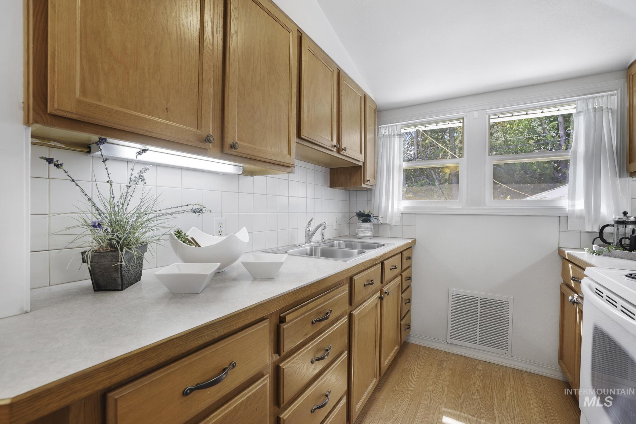Kitchen featuring light countertops, tasteful backsplash, light wood-type flooring, brown cabinets, and white range with electric stovetop