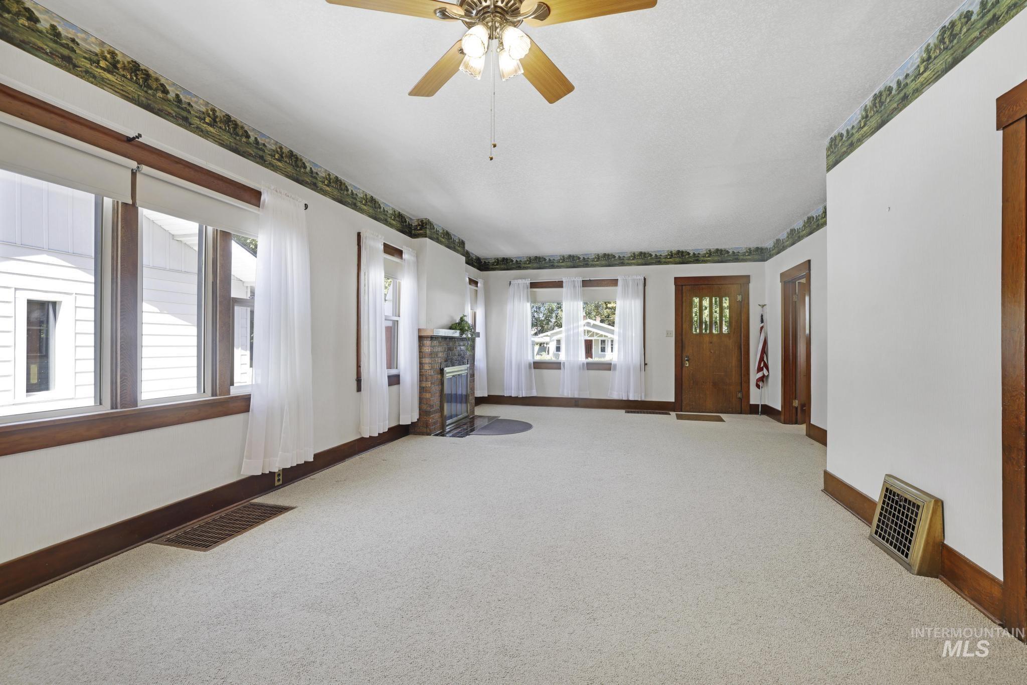 Carpeted spare room featuring a fireplace with flush hearth and a ceiling fan