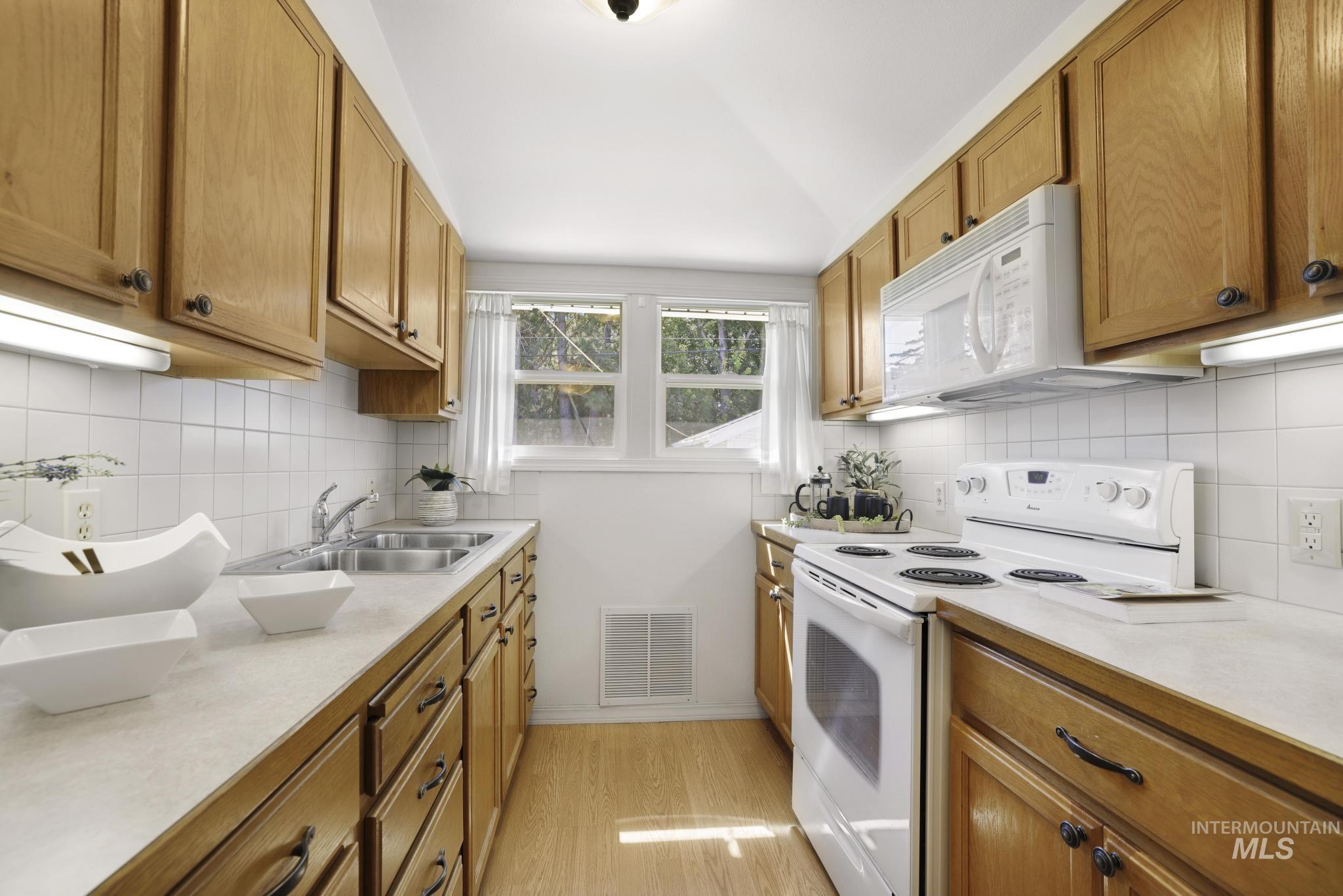 Kitchen featuring white appliances, light countertops, light wood-style flooring, and brown cabinets
