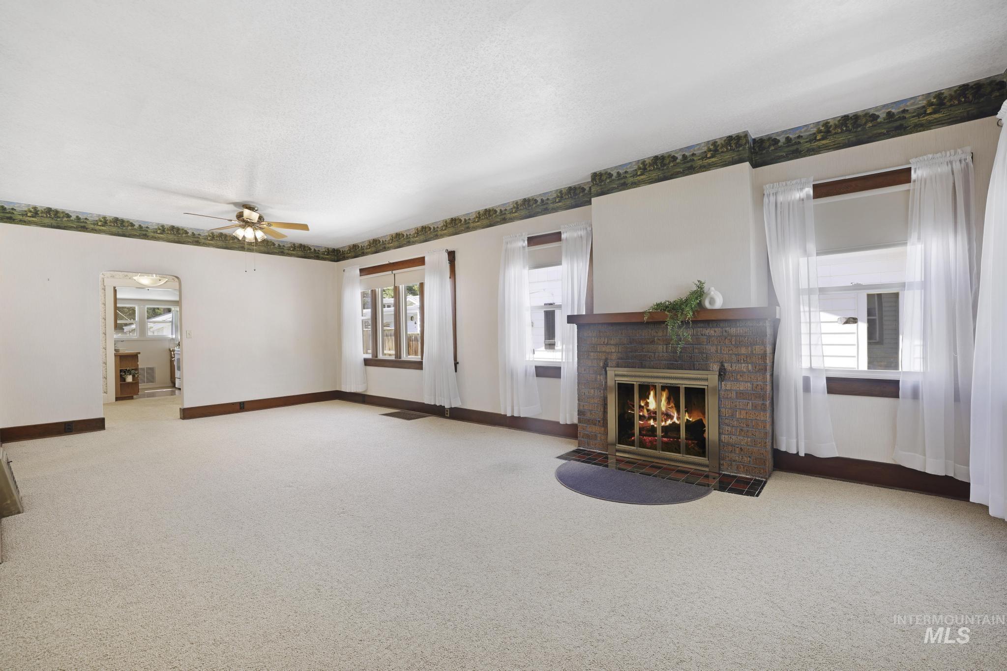 Unfurnished living room featuring a fireplace, light colored carpet, plenty of natural light, ceiling fan, and a textured ceiling