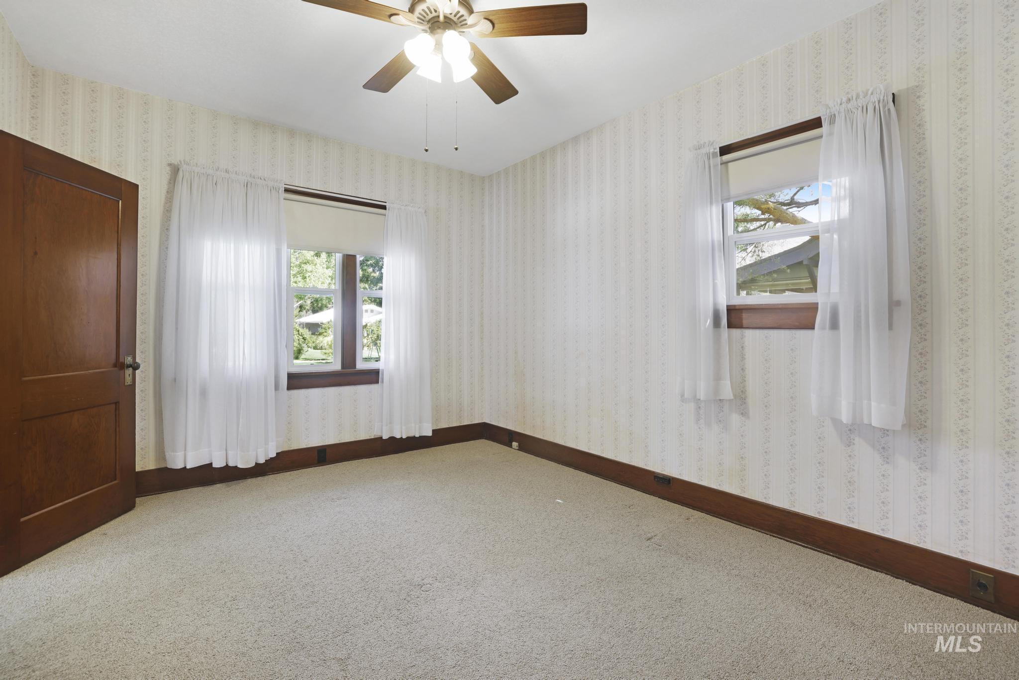 Spare room featuring light carpet, wallpapered walls, and ceiling fan