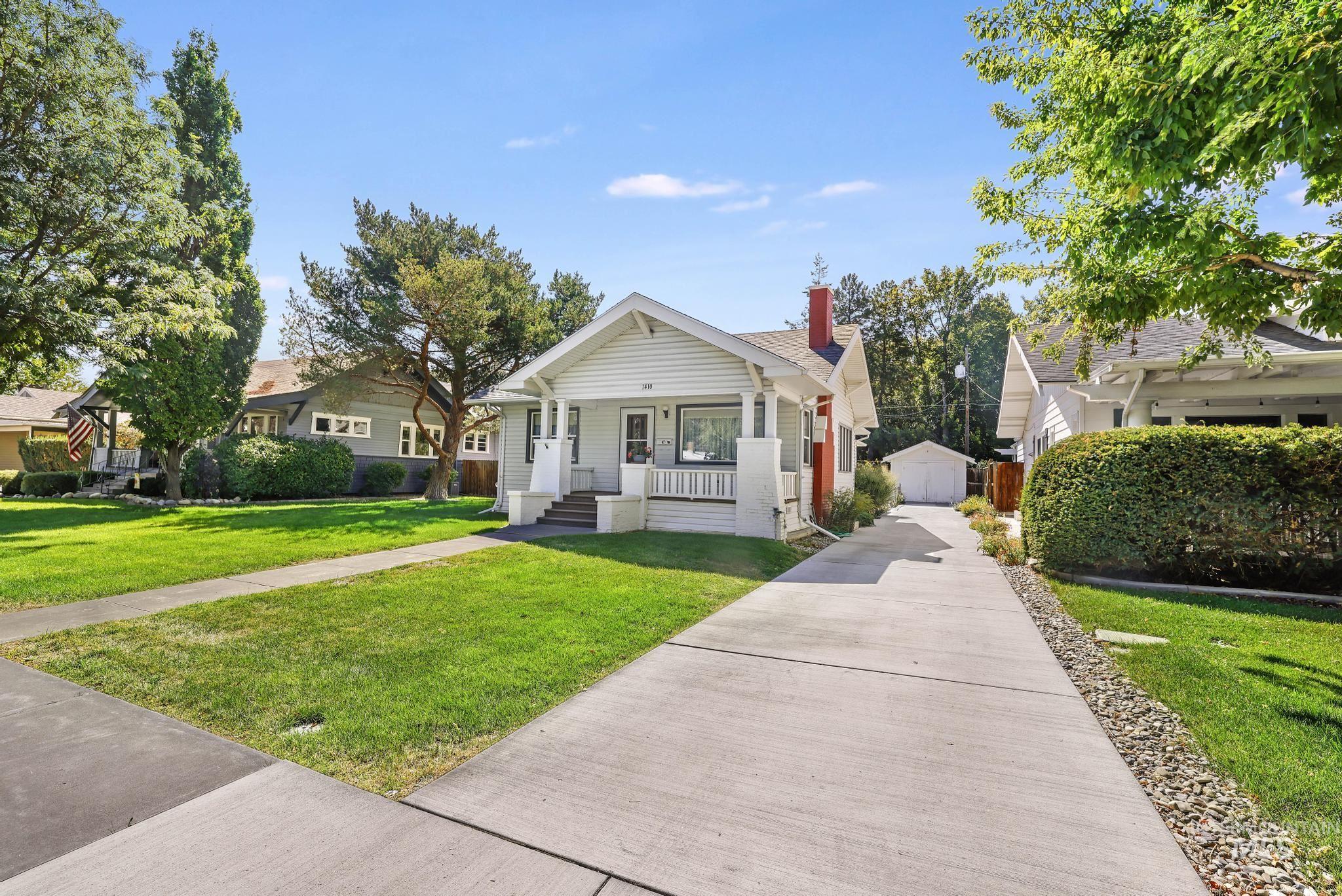 Bungalow-style home with a porch, a chimney, a front lawn, and an outbuilding