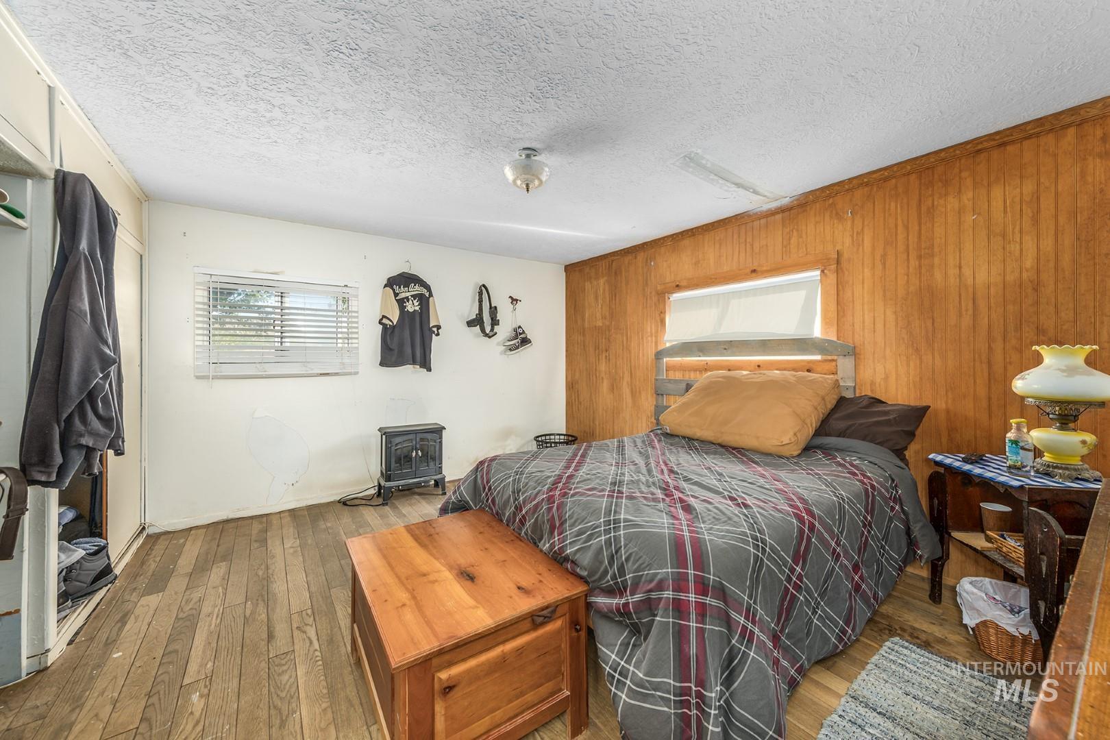 Bedroom with hardwood / wood-style floors, wood walls, a textured ceiling, and a wood stove