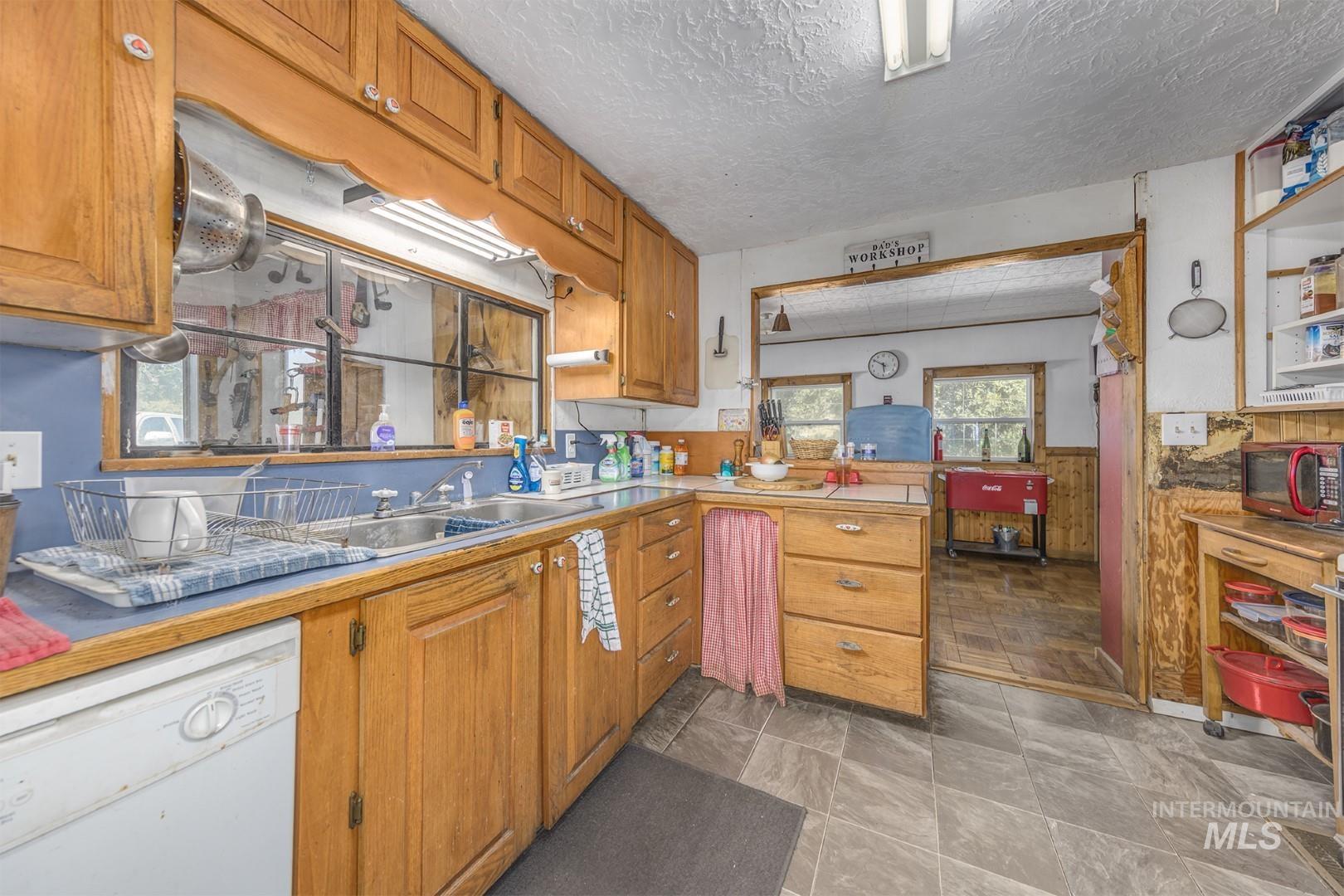 Kitchen with white dishwasher, wooden walls, light countertops, brown cabinets, and wainscoting