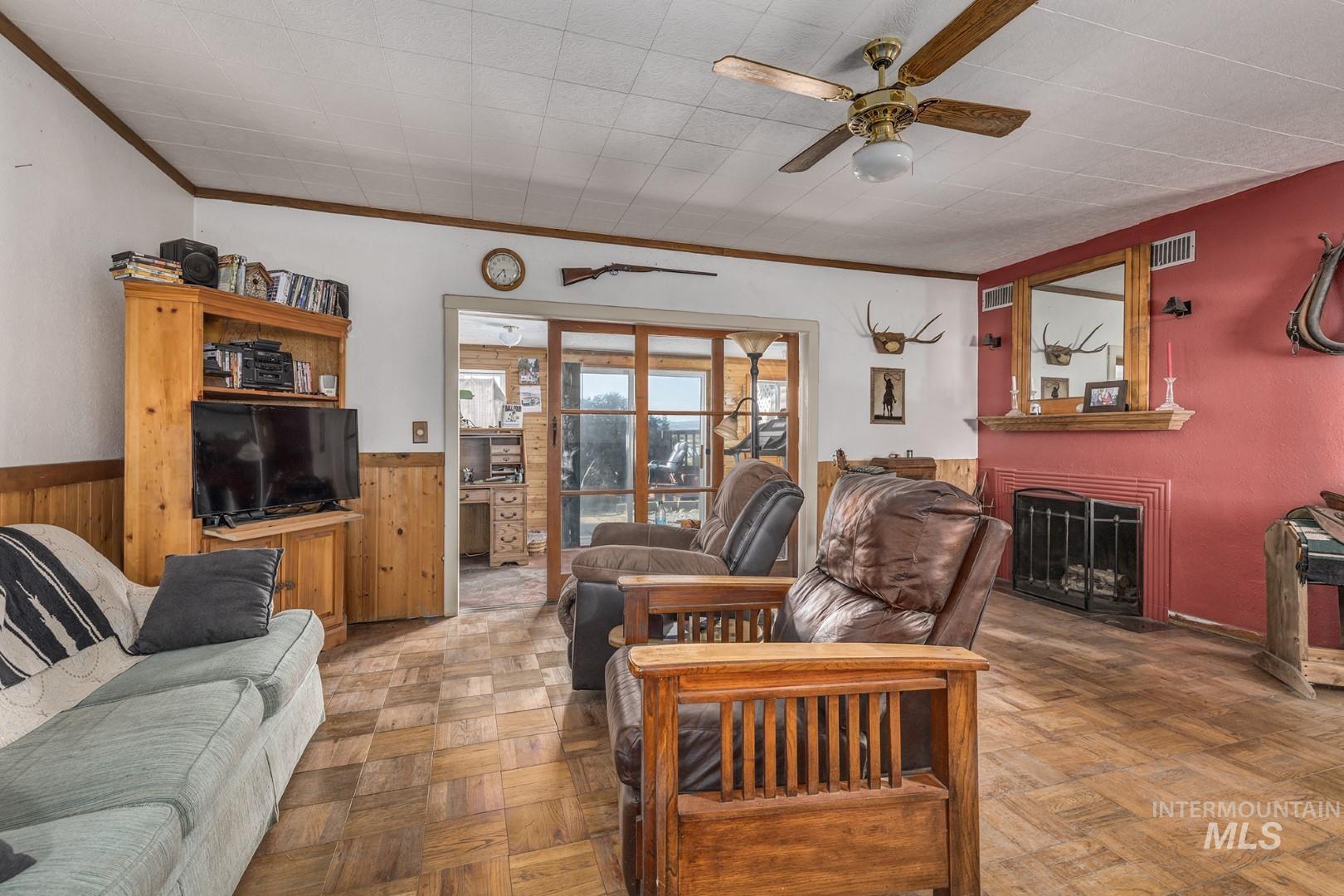 Living room with ornamental molding, a fireplace, a ceiling fan, and wooden walls