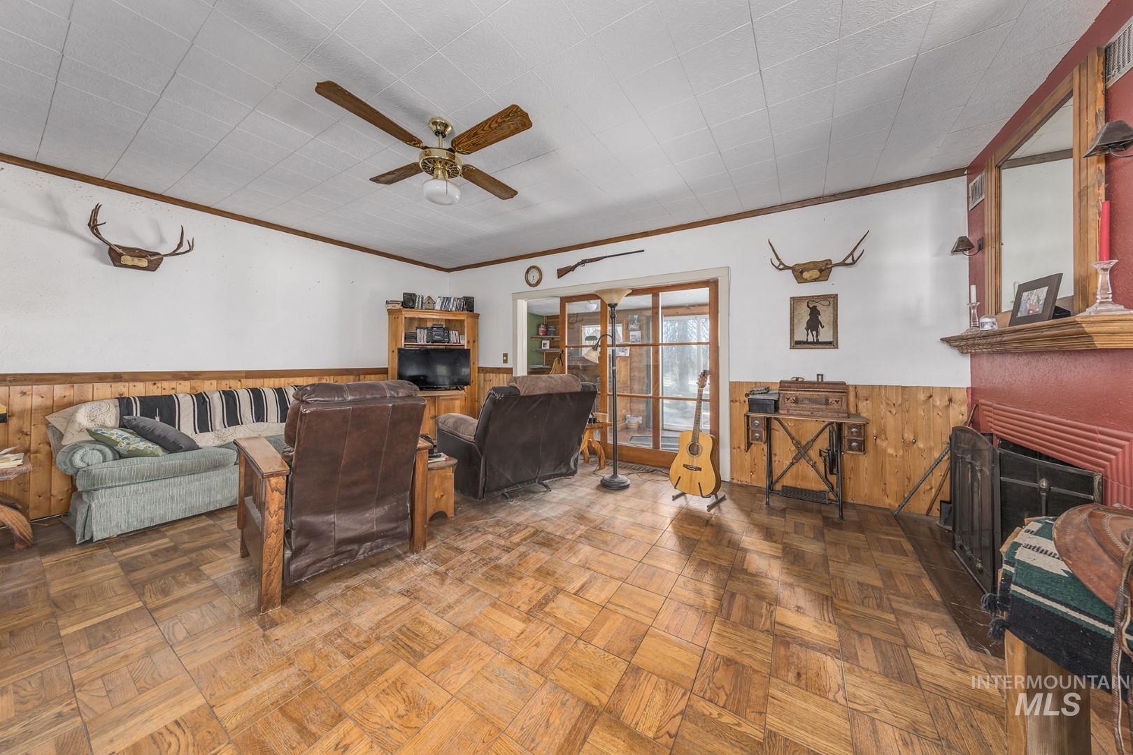 Living room with wood walls, wainscoting, crown molding, a fireplace, and ceiling fan