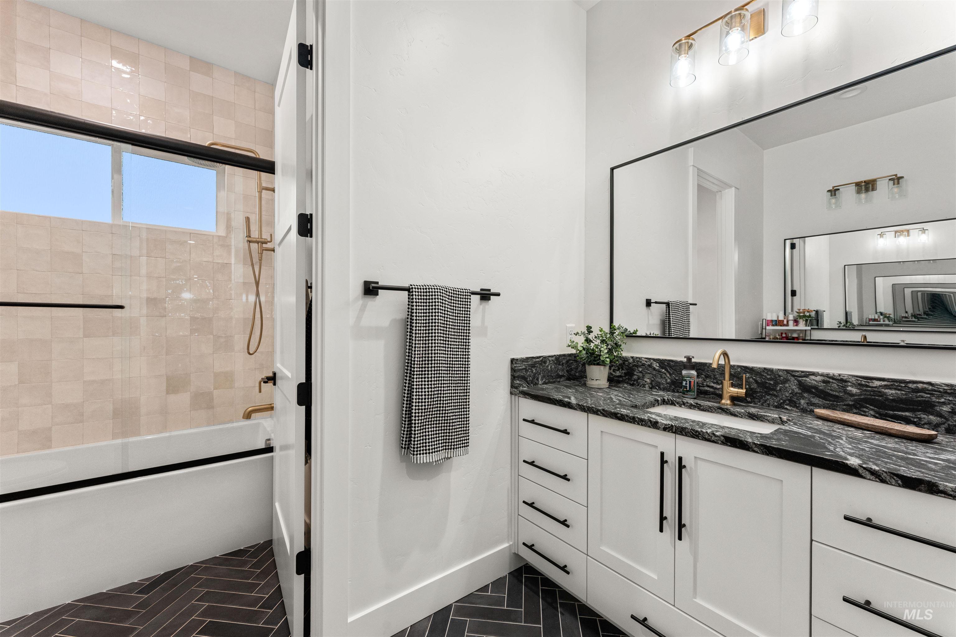Full bathroom with combined bath / shower with glass door, vanity, and dark tile patterned floors