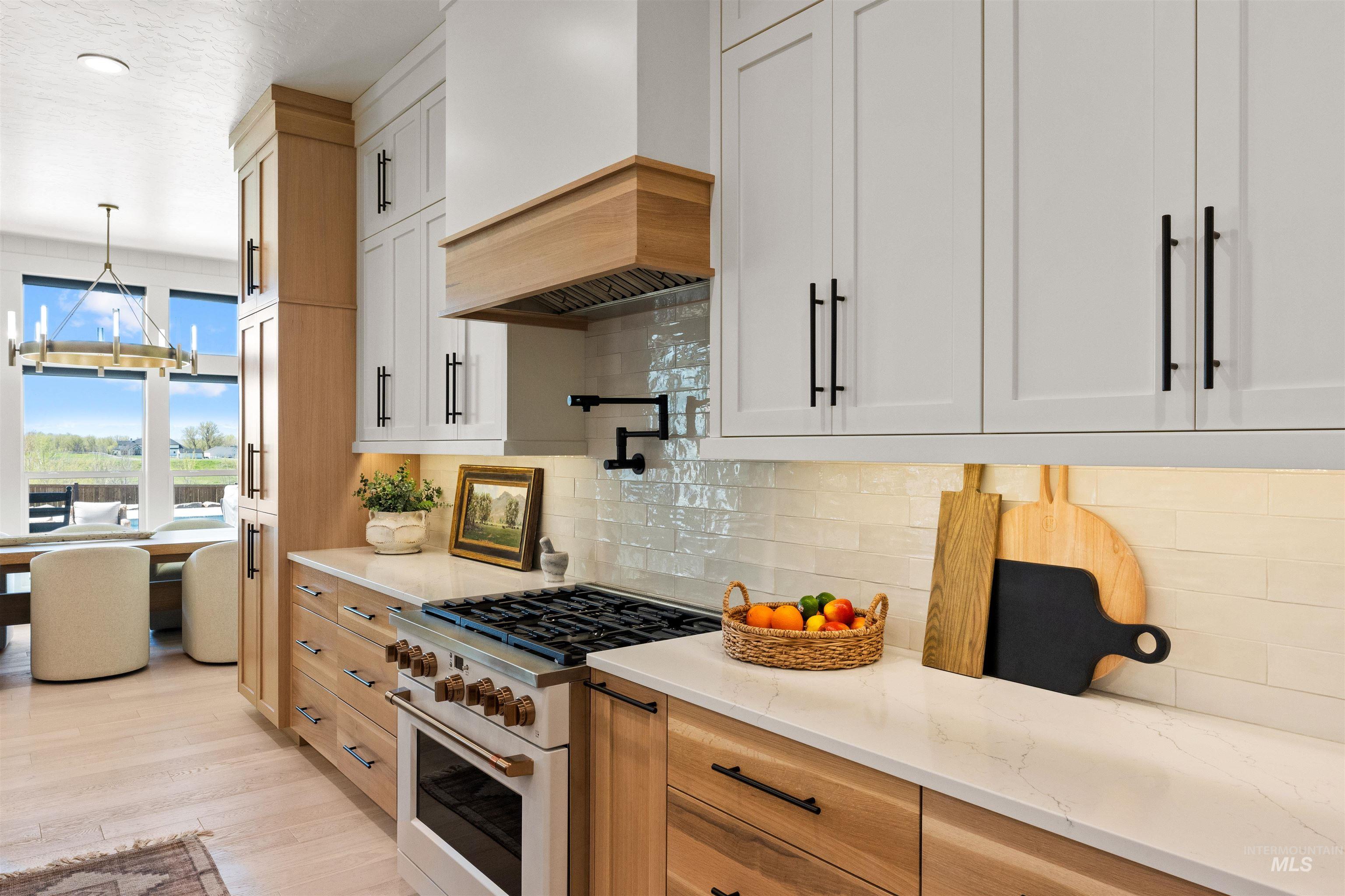 Kitchen with high end white range, light stone countertops, tasteful backsplash, light wood-style floors, and custom exhaust hood