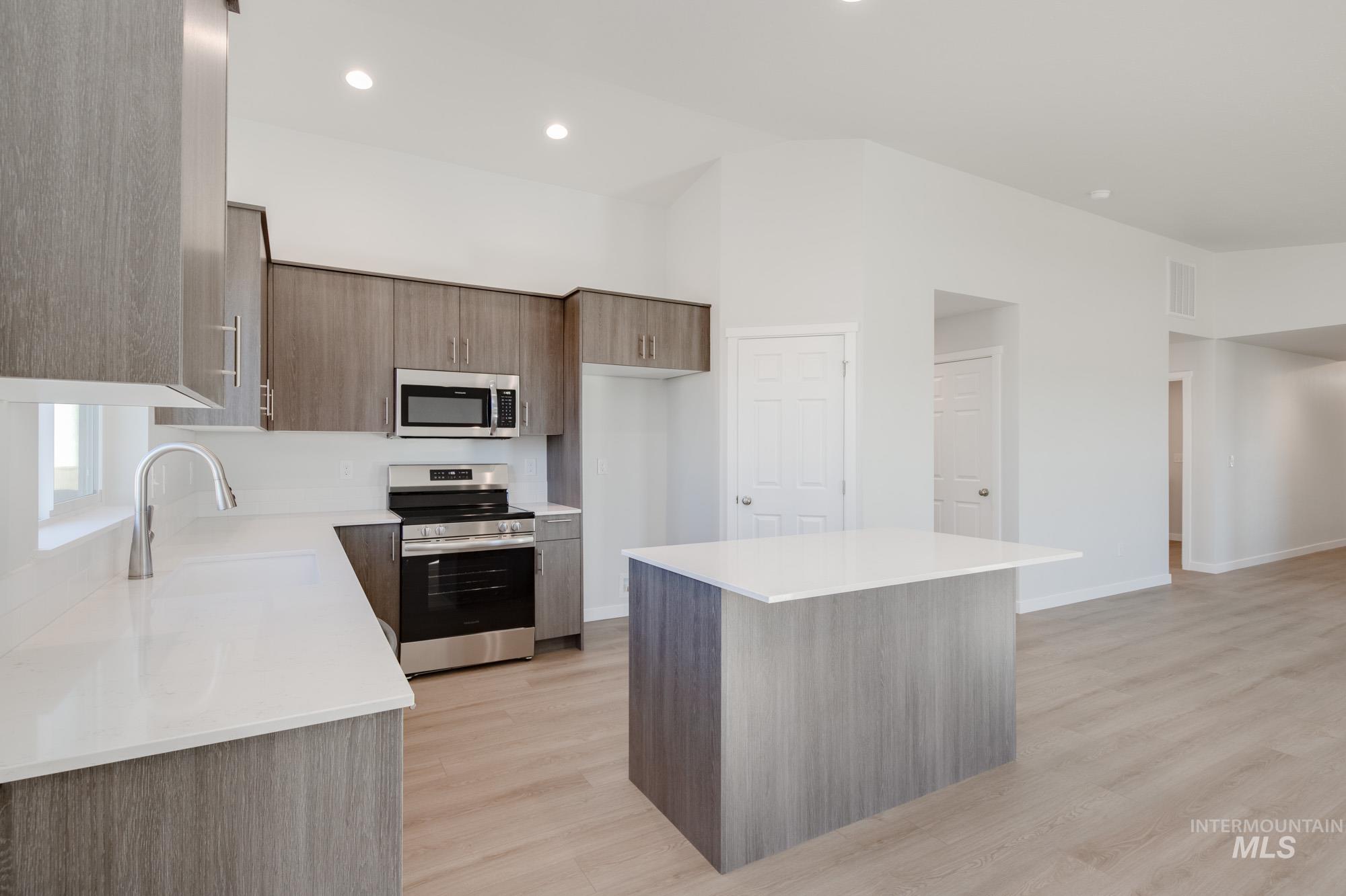 Kitchen featuring stainless steel appliances, a center island, modern cabinets, light stone counters, and light wood finished floors