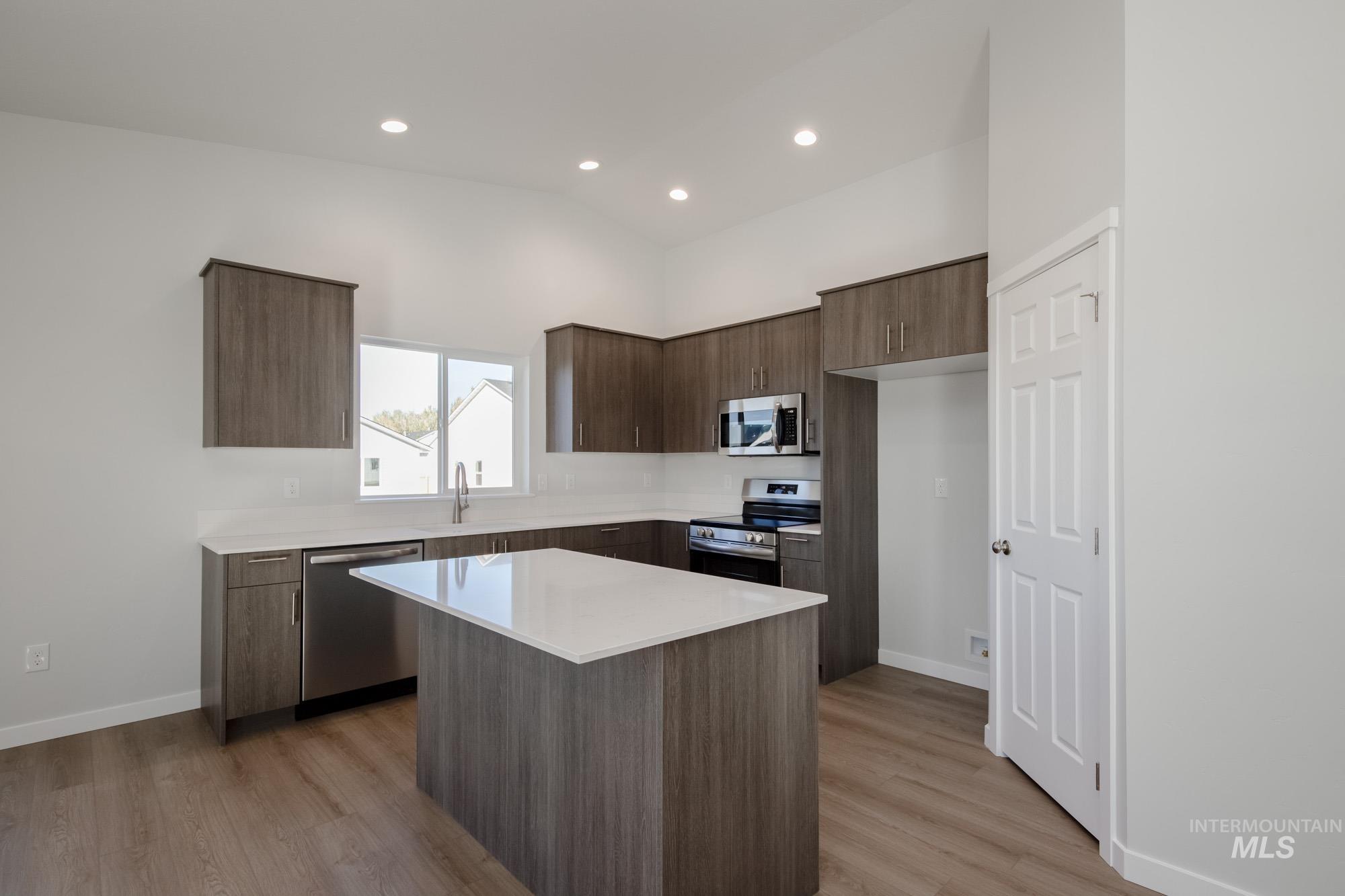 Kitchen featuring dark brown cabinetry, stainless steel appliances, modern cabinets, a center island, and light wood finished floors