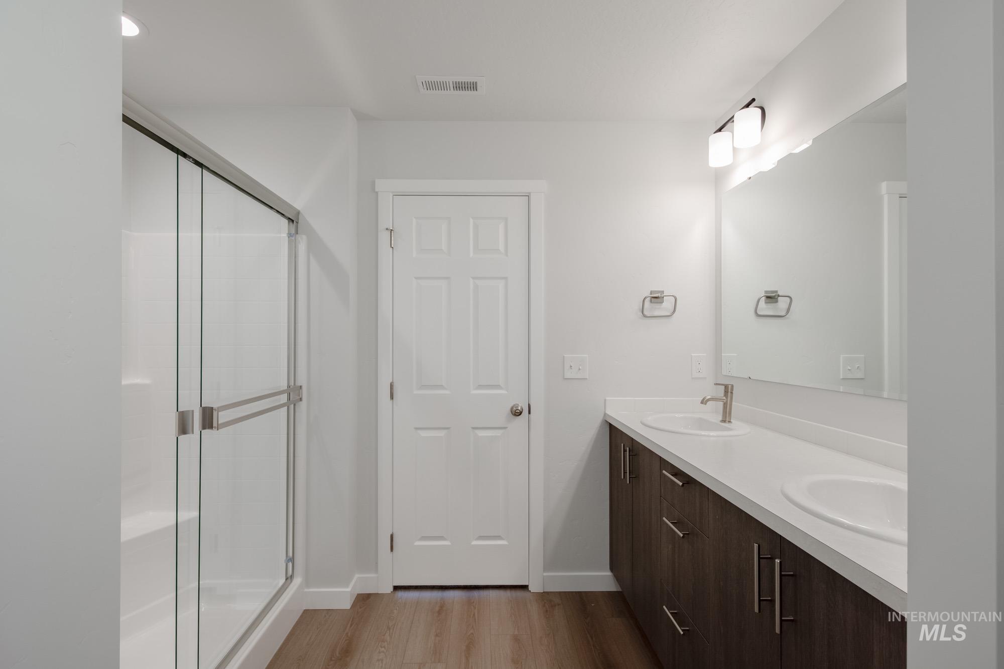Bathroom featuring light wood finished floors, double vanity, a stall shower, and recessed lighting