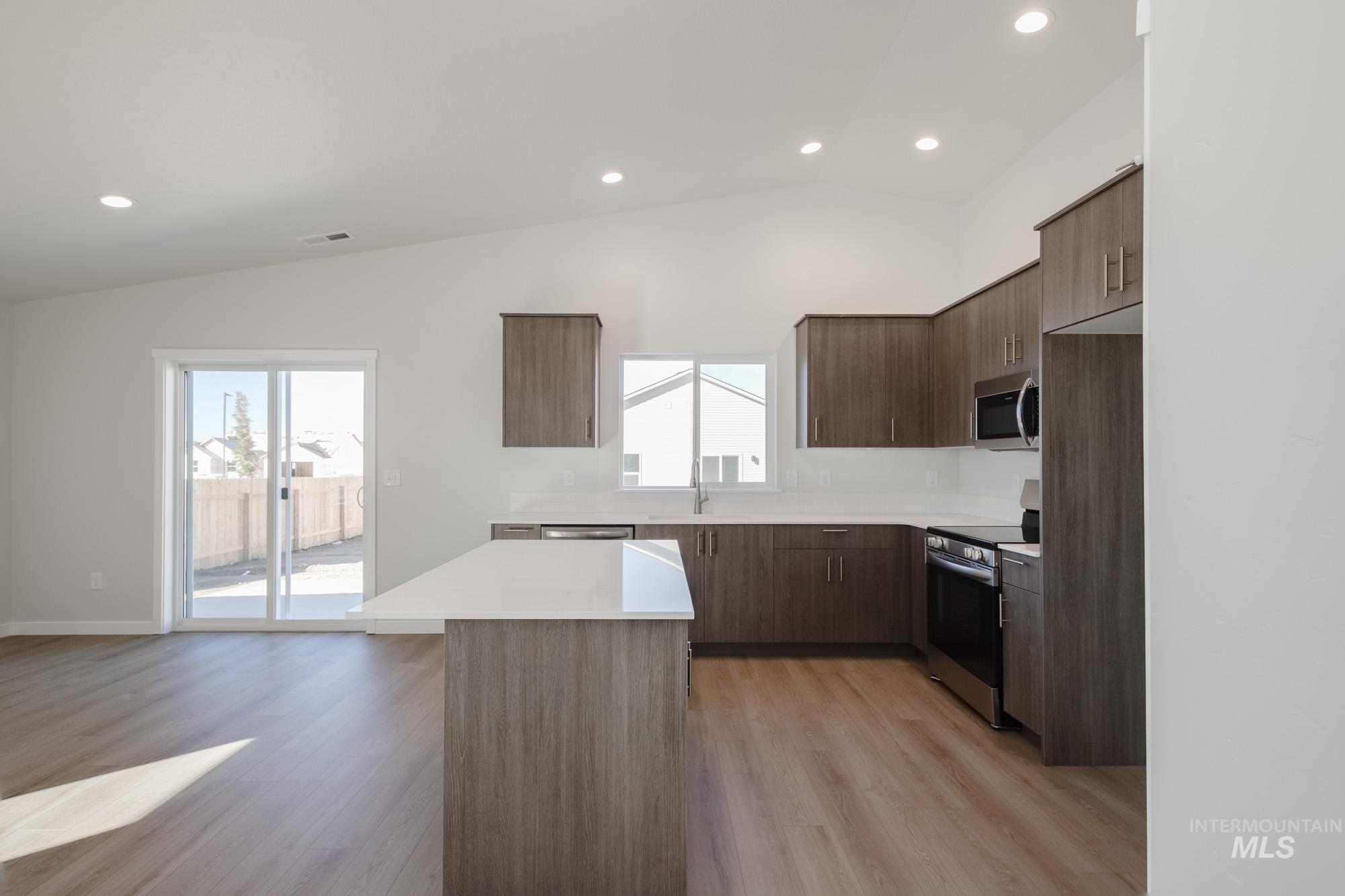 Kitchen featuring modern cabinets, appliances with stainless steel finishes, recessed lighting, lofted ceiling, and light wood-style floors