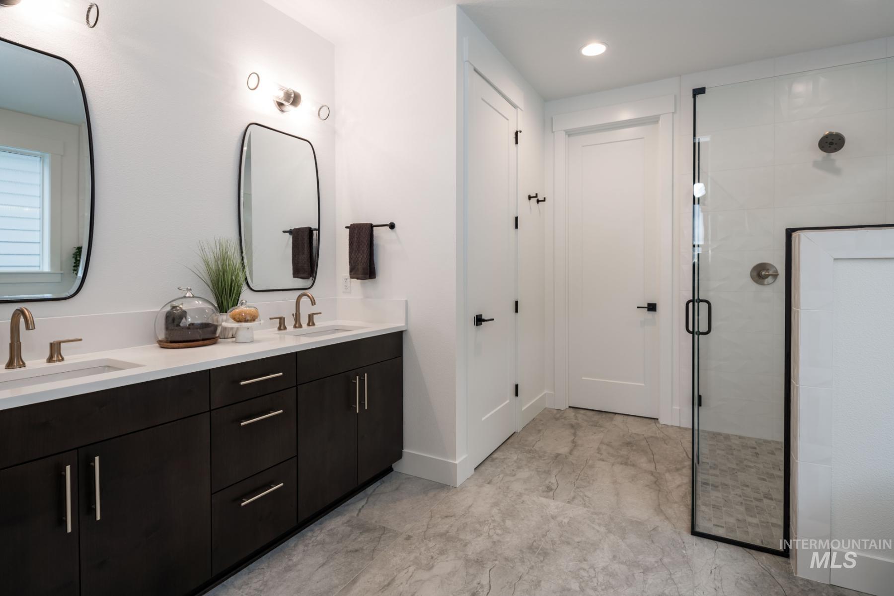 Full bath featuring double vanity, a shower stall, recessed lighting, and light marble finish flooring