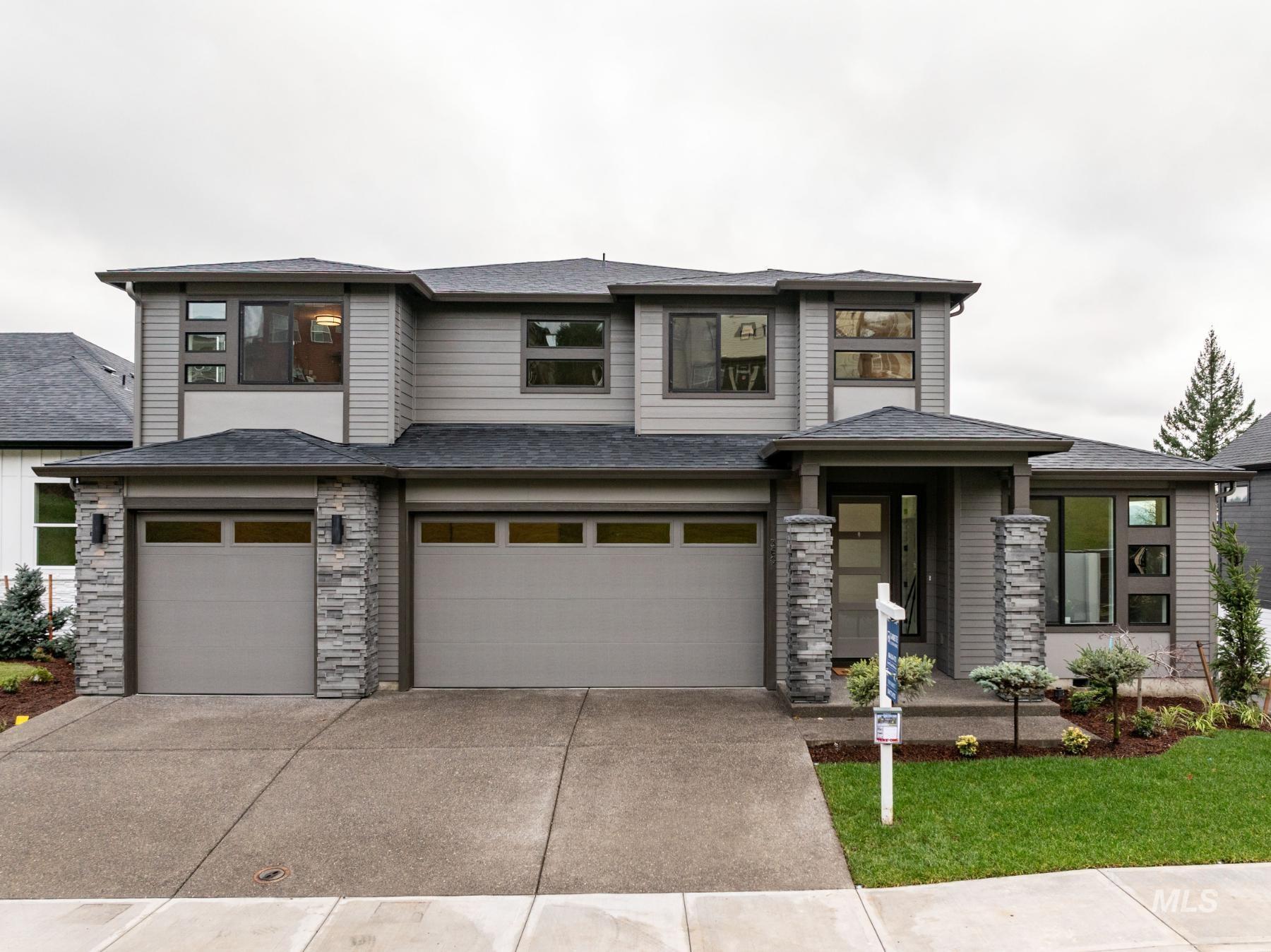 Prairie-style home featuring driveway, an attached garage, stone siding, a front lawn, and roof with shingles