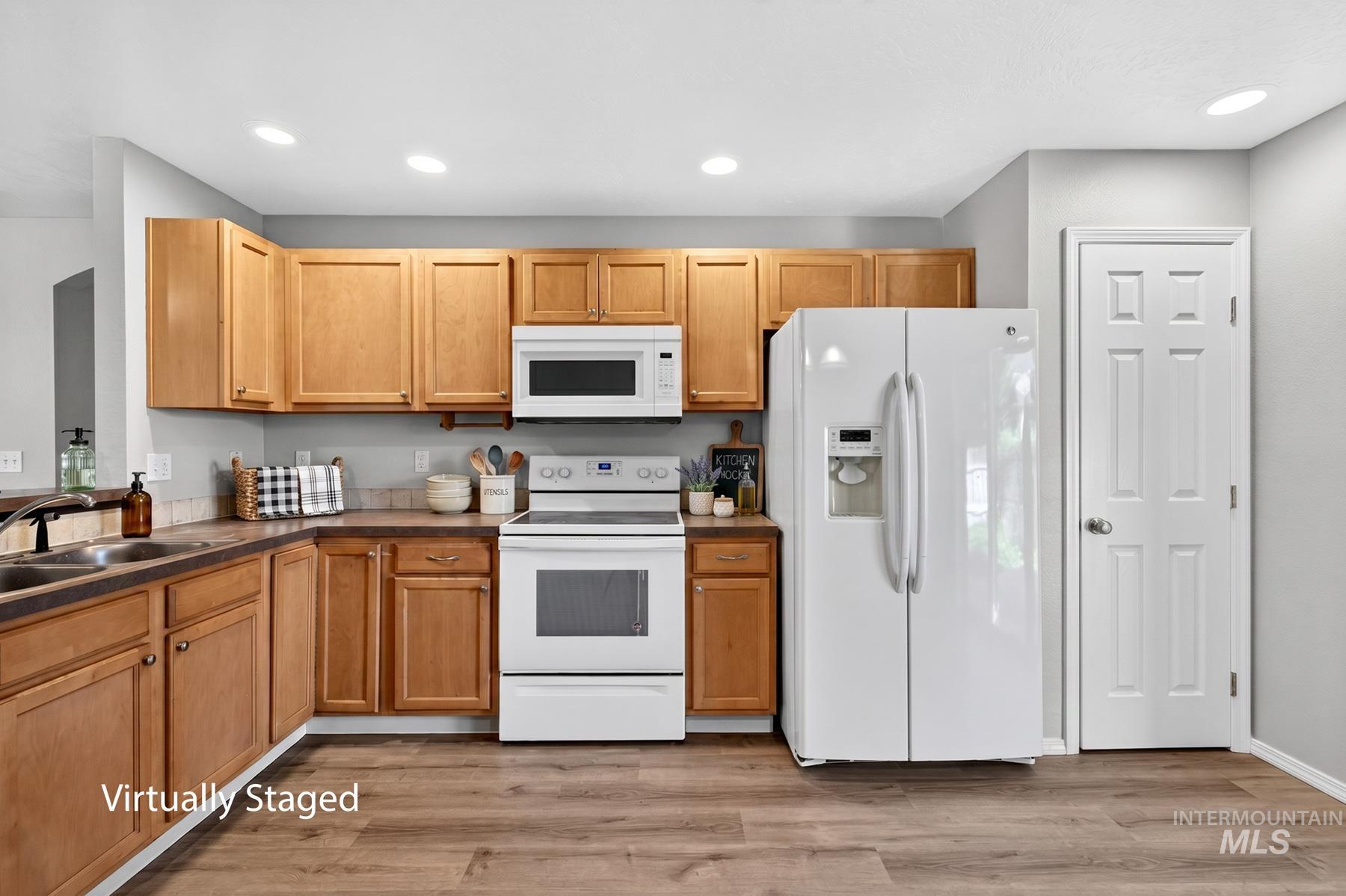 Kitchen featuring light wood cabinetry, white appliances, recessed lighting, wood-finish flooring, and a double basin sink