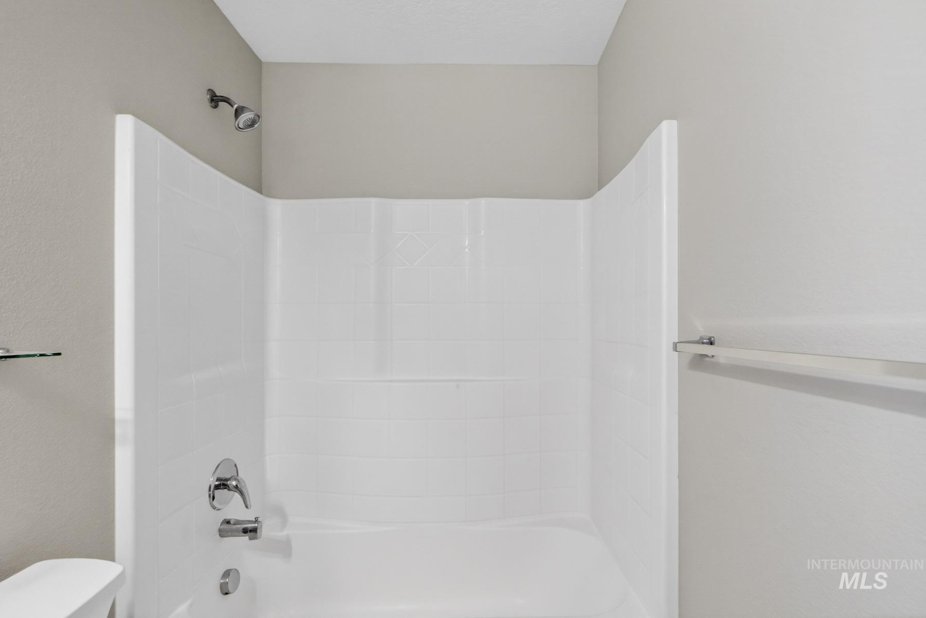 White tub and shower combination with a curved surround, chrome fixtures, and a wall-mounted showerhead