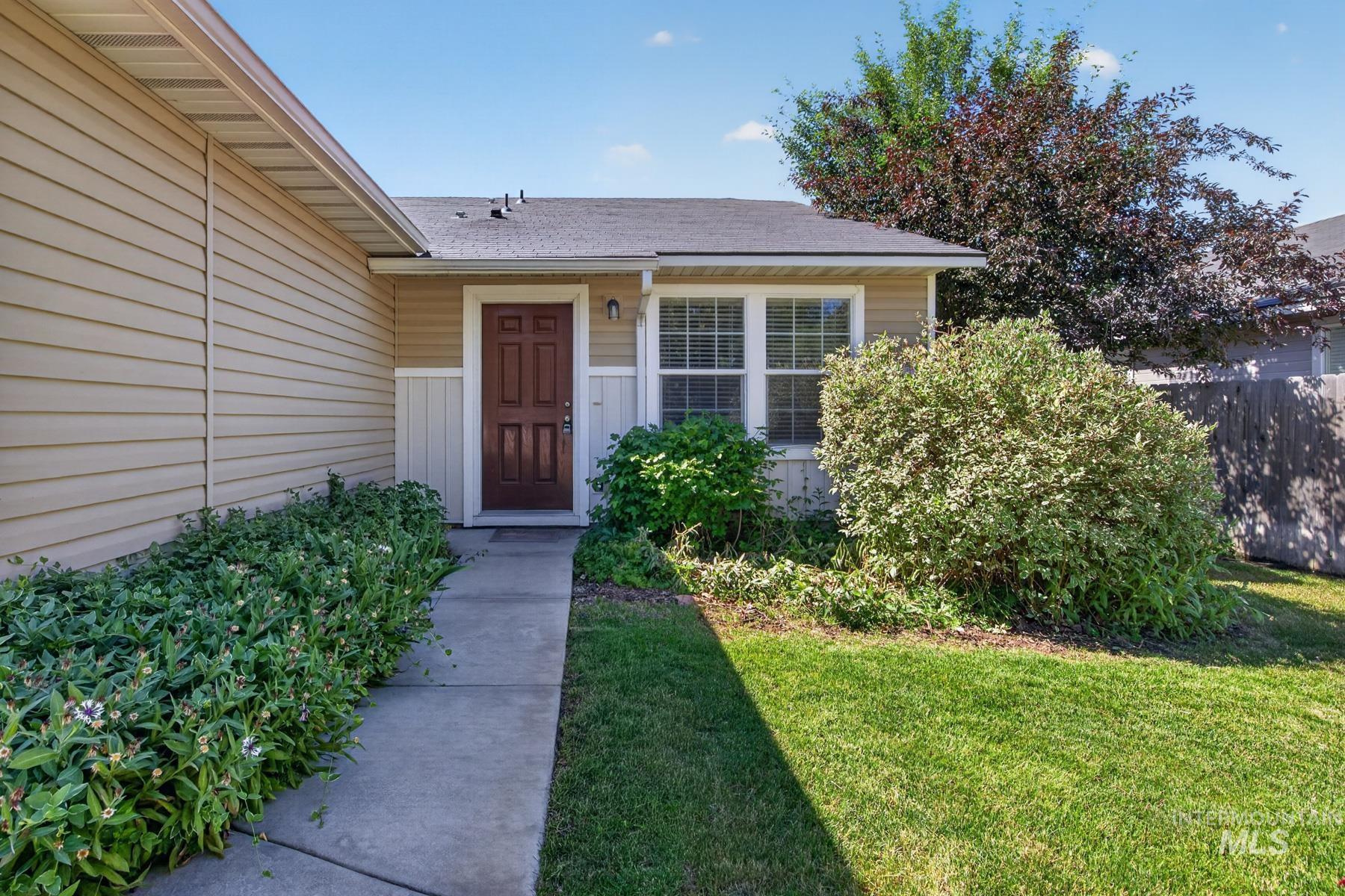 Entryway featuring a paneled wood door, a concrete pathway, a window with white framing, and established shrubbery
