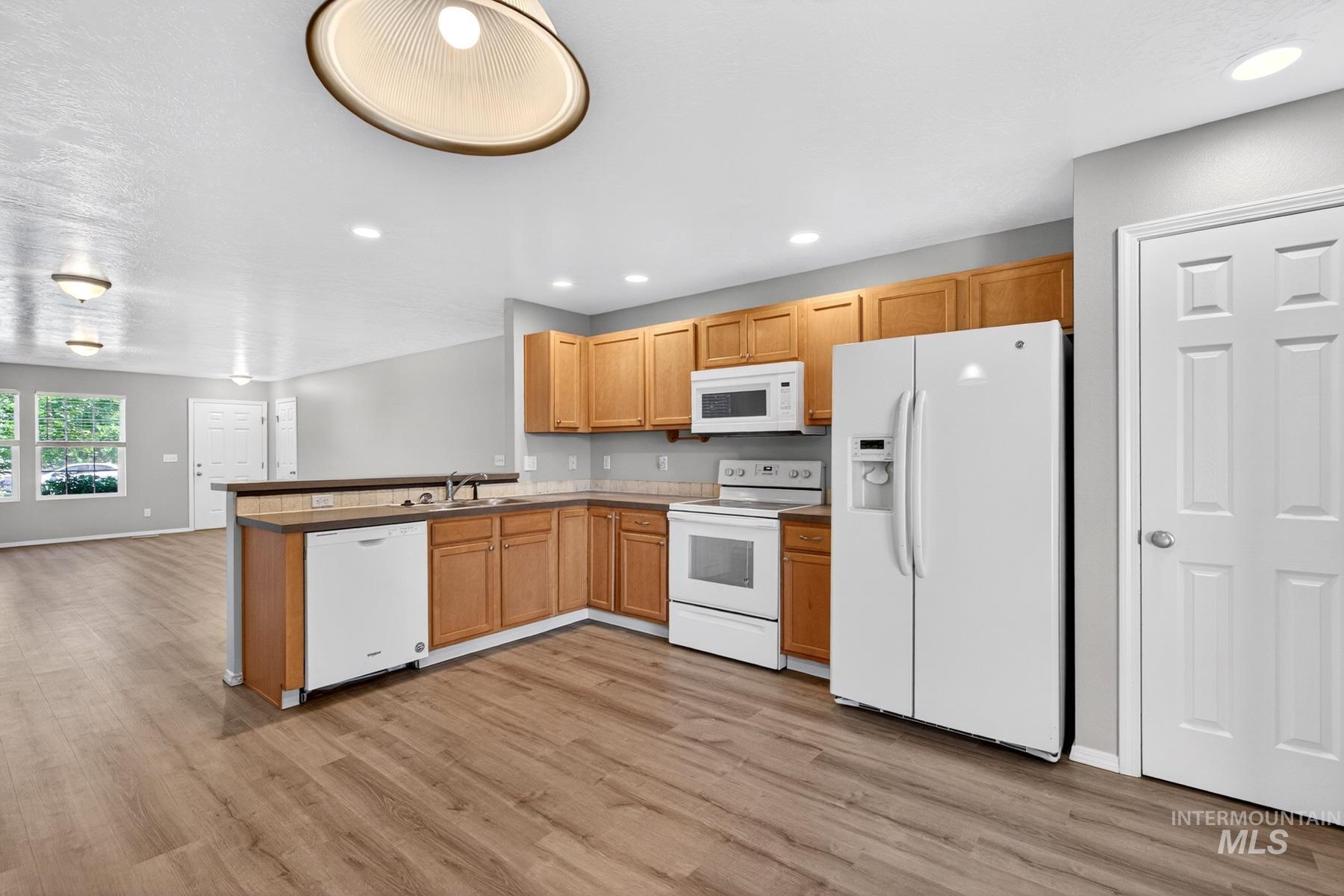 Open concept kitchen featuring wood-finish flooring, light wood cabinetry, and a white appliance suite including a refrigerator, microwave, range, and dishwasher