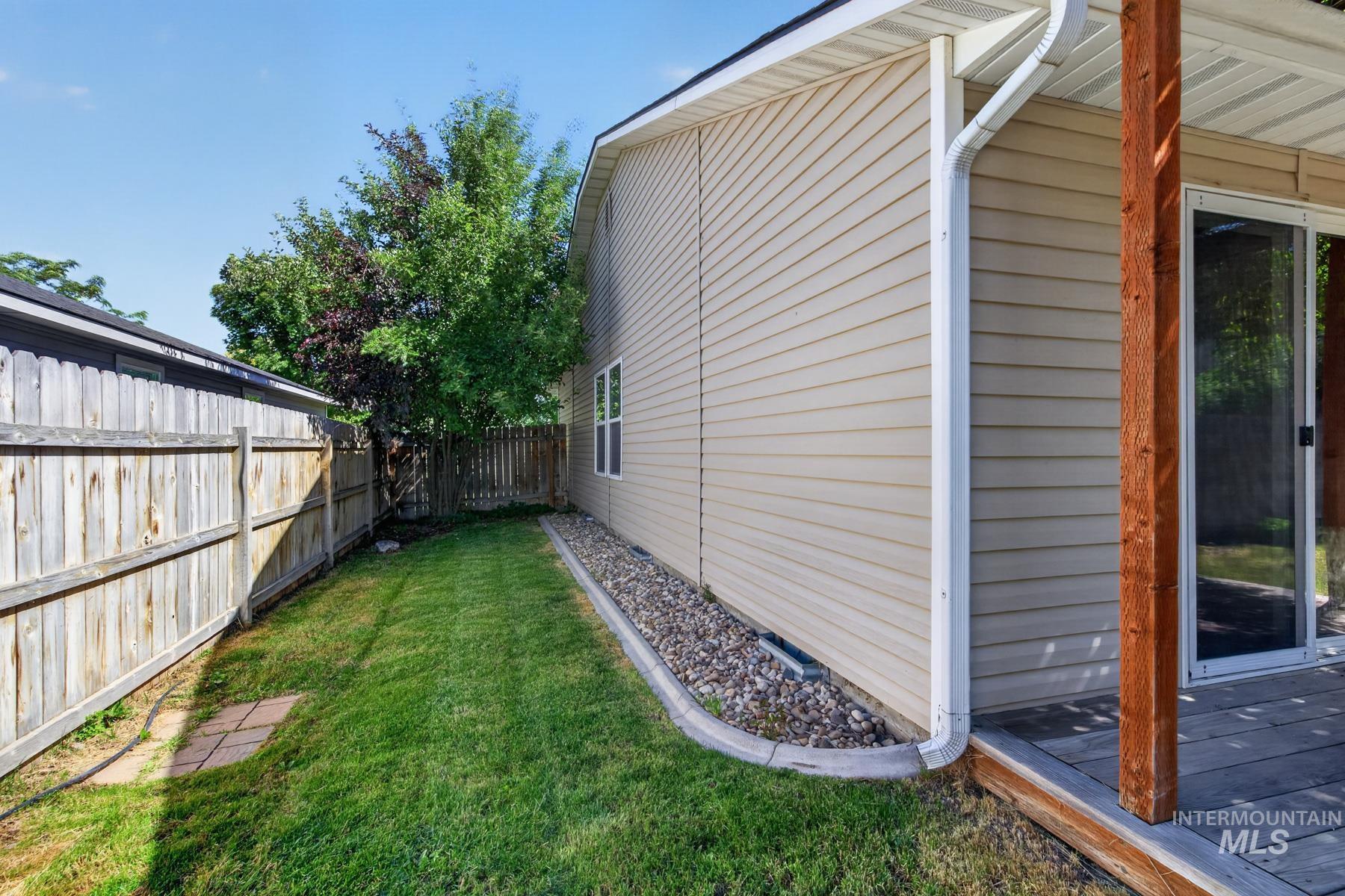 Expansive side yard featuring a manicured lawn, wood fencing, and mature trees