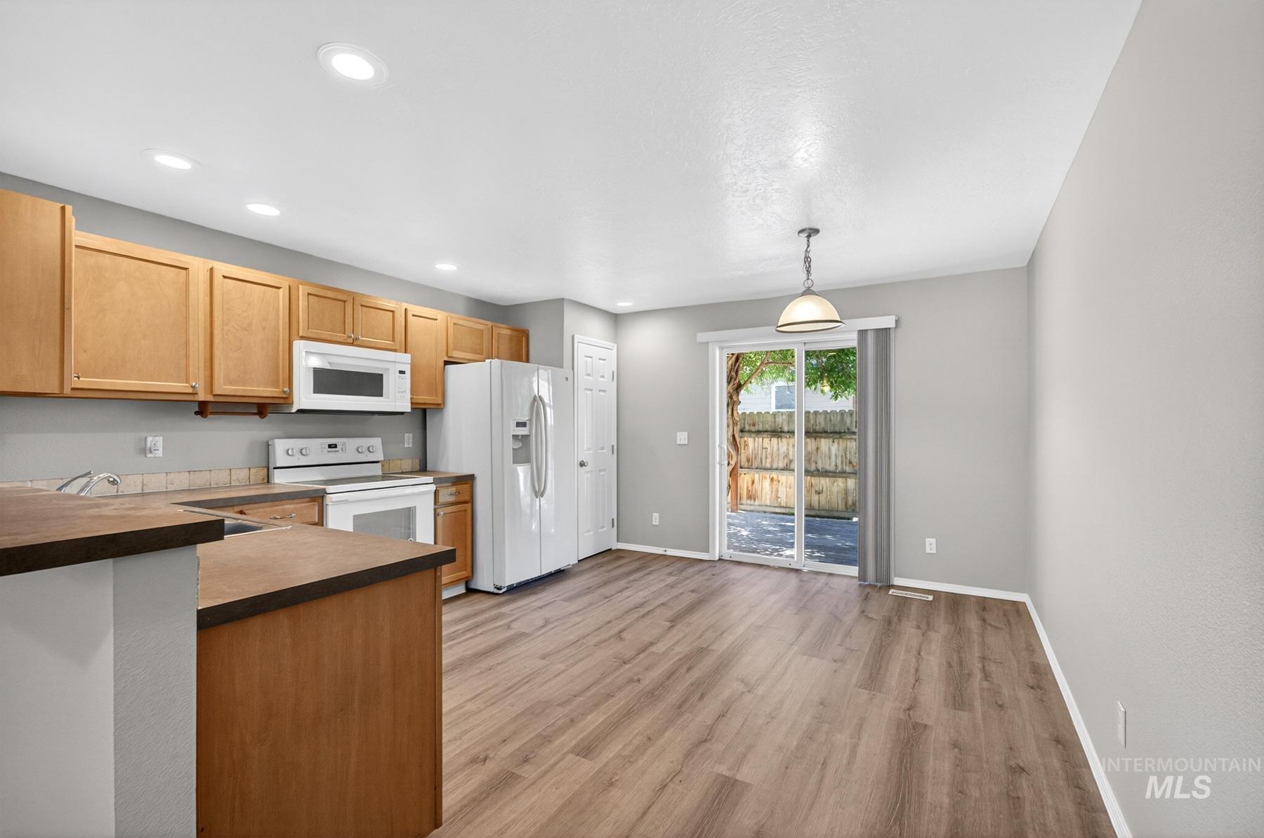 Open-concept kitchen with light wood cabinetry, white appliances, and wood-finish flooring