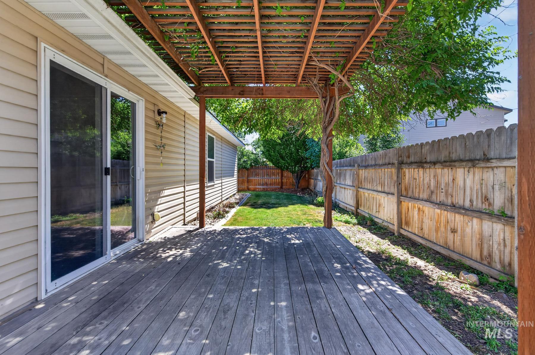Wood deck with overhead pergola, beige vinyl siding, sliding glass door, and a wooden privacy fence