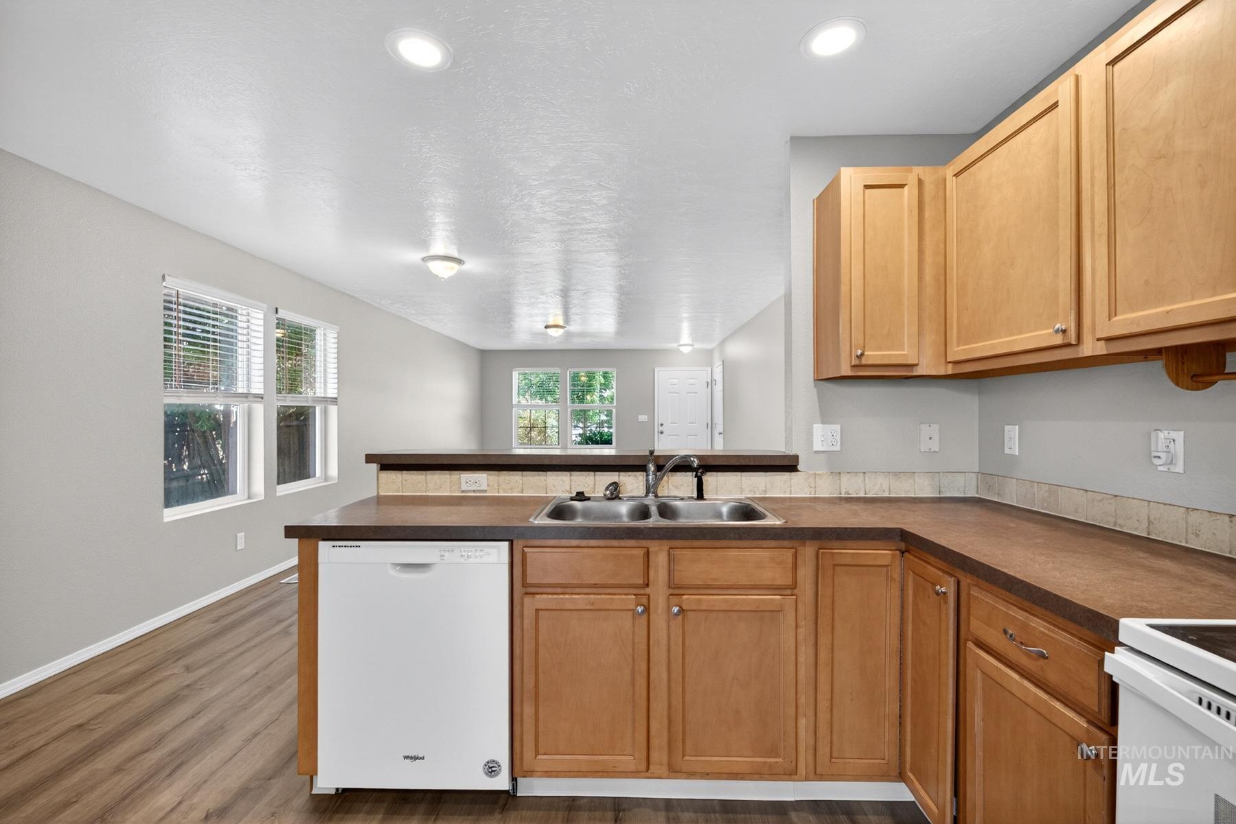 Kitchen featuring wood-finish cabinetry, a double basin sink, and a white dishwasher