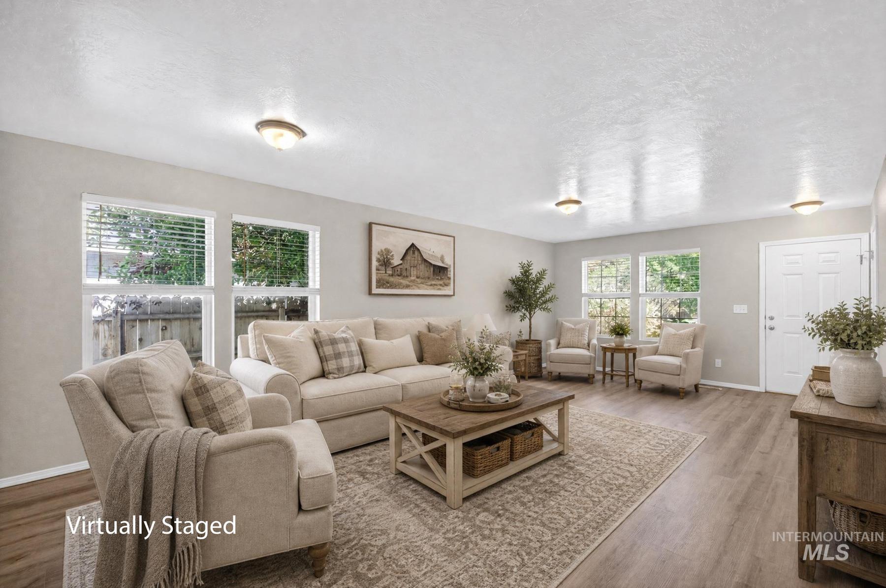Spacious living area featuring light-toned walls, wood-finish flooring, and multiple large windows