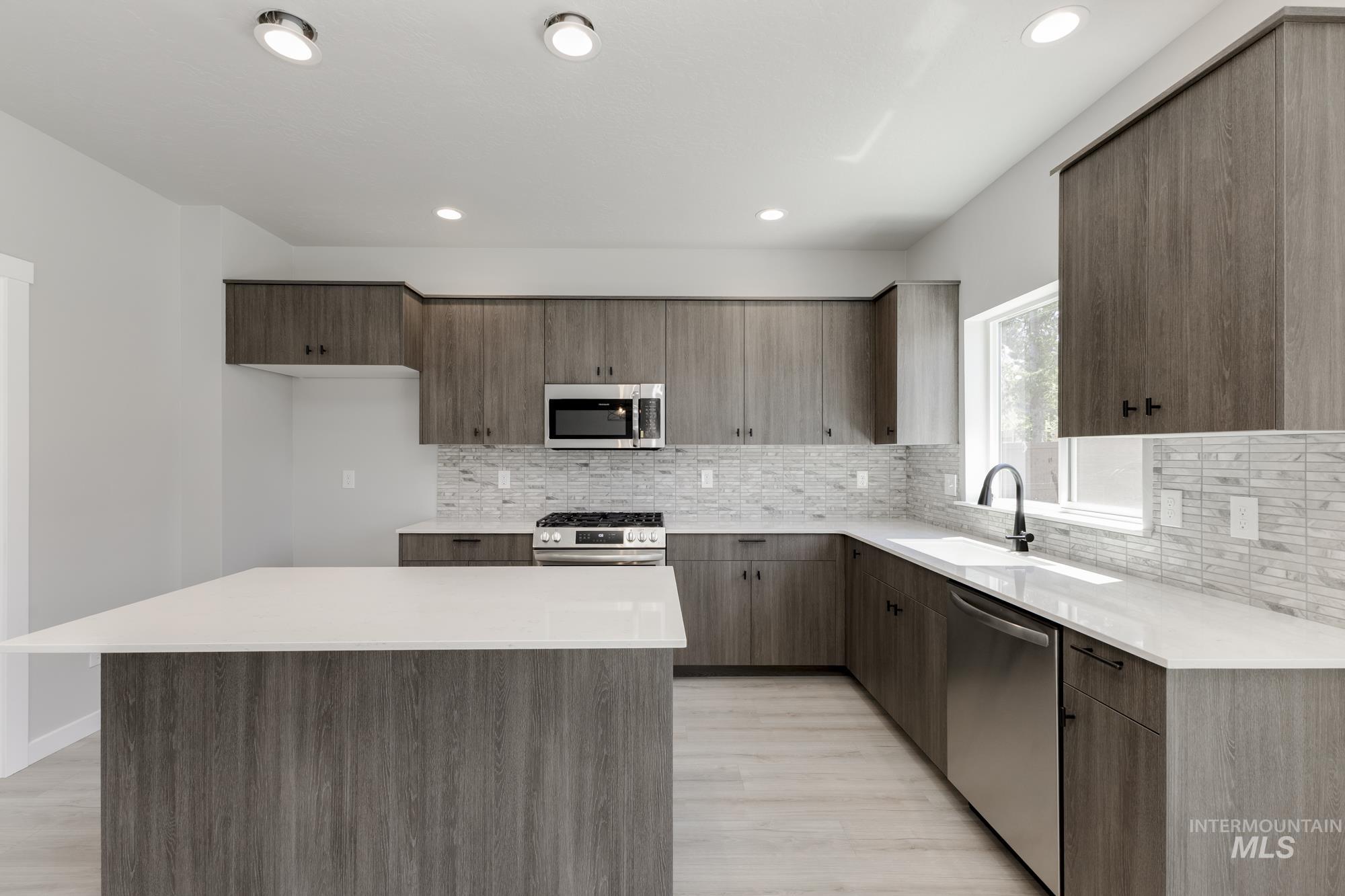 Kitchen with appliances with stainless steel finishes, light wood-style flooring, backsplash, light countertops, and a center island