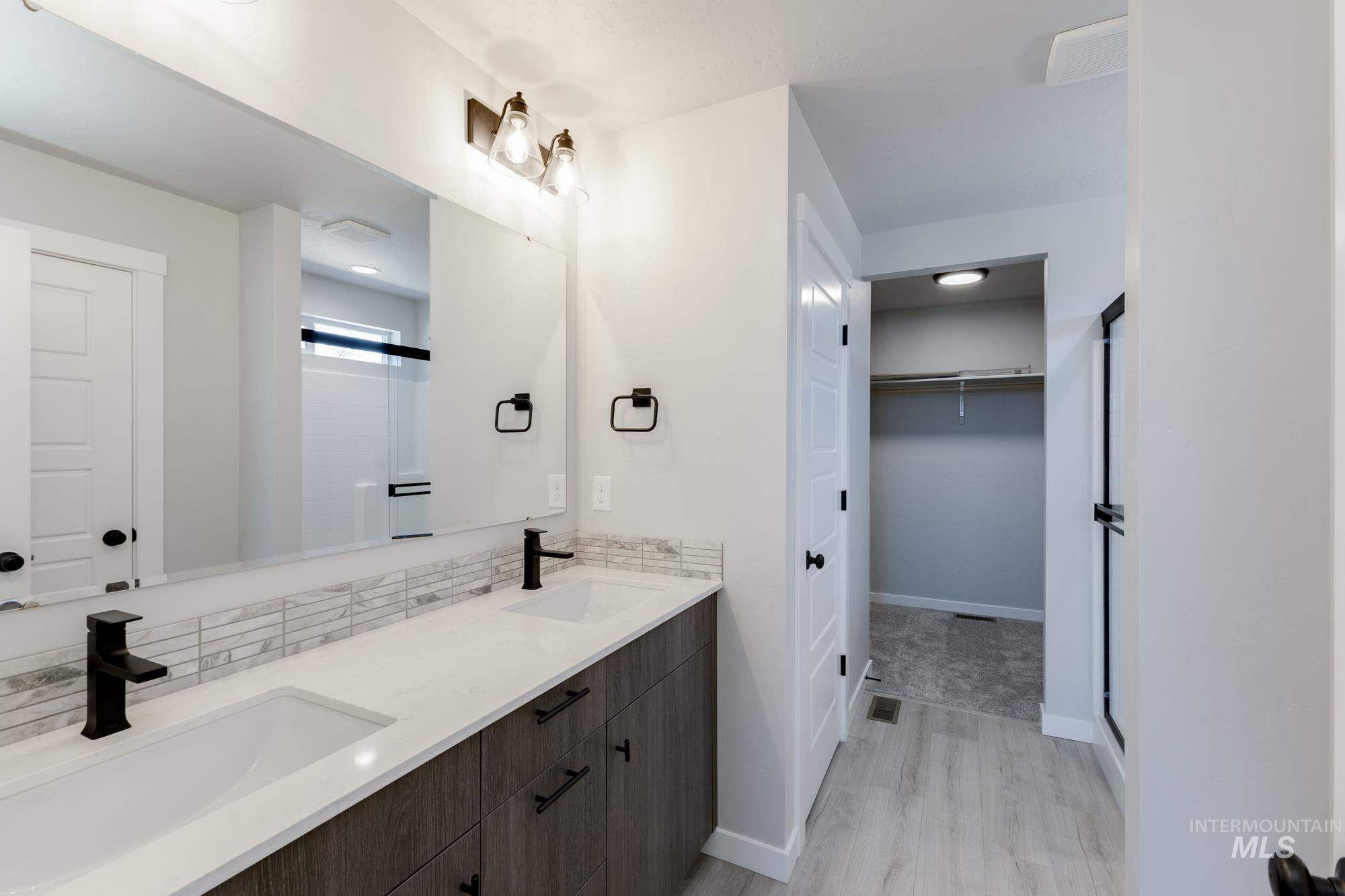 Bathroom featuring double vanity, wood finished floors, a spacious closet, and decorative backsplash