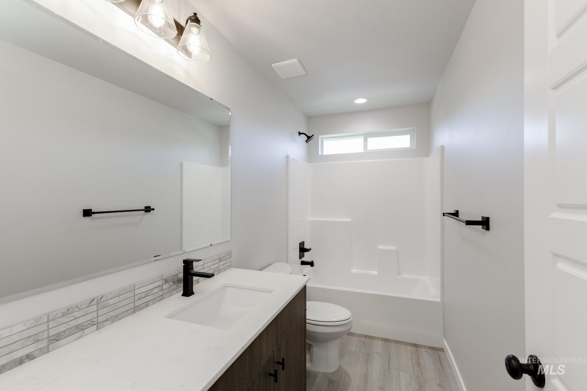 Full bath with vanity, tub / shower combination, wood finished floors, and tasteful backsplash