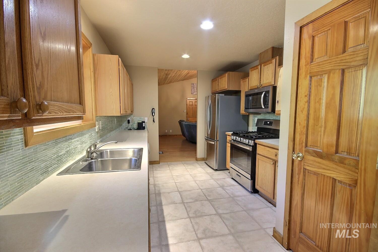 Kitchen with stainless steel appliances, backsplash, light countertops, recessed lighting, and light brown cabinets