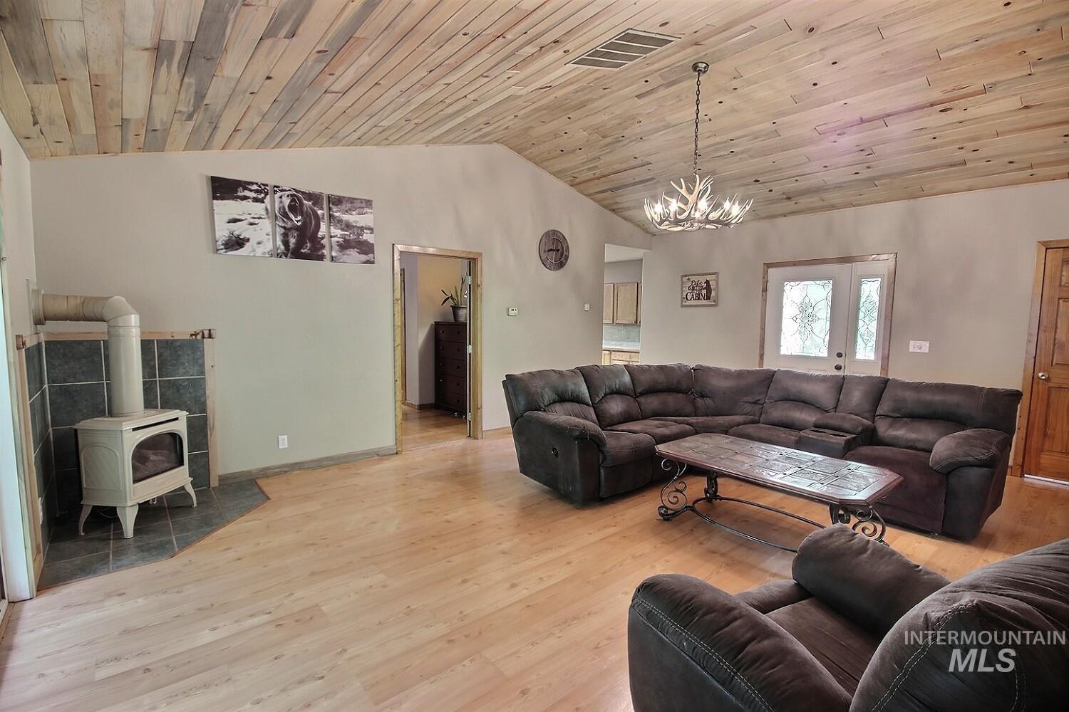 Living room featuring light wood-style flooring, a wood stove, a chandelier, wood ceiling, and high vaulted ceiling