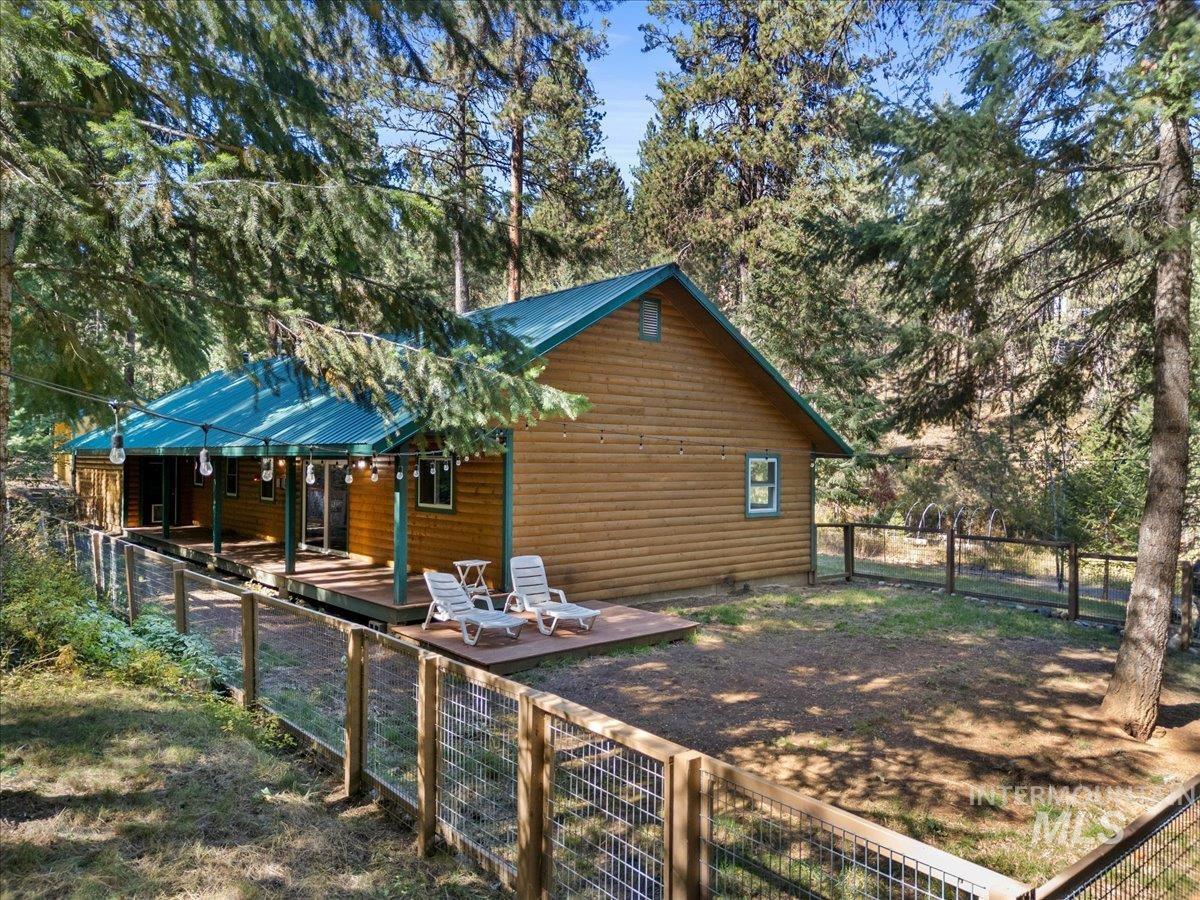 View of side of property featuring a gate, a fenced backyard, faux log siding, and a metal roof