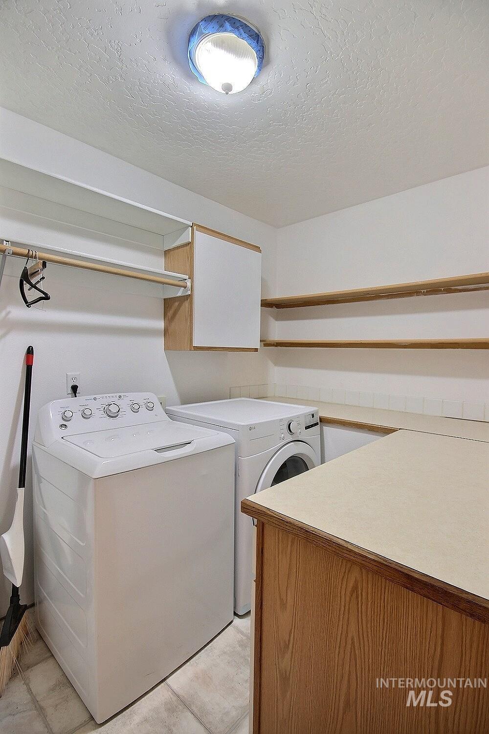Laundry room with cabinet space, a textured ceiling, light tile patterned floors, and washing machine and clothes dryer