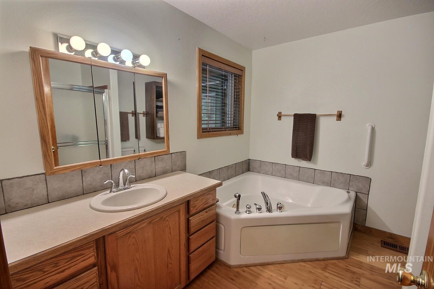 Bathroom with vanity, a bath, light wood-style flooring, a stall shower, and backsplash