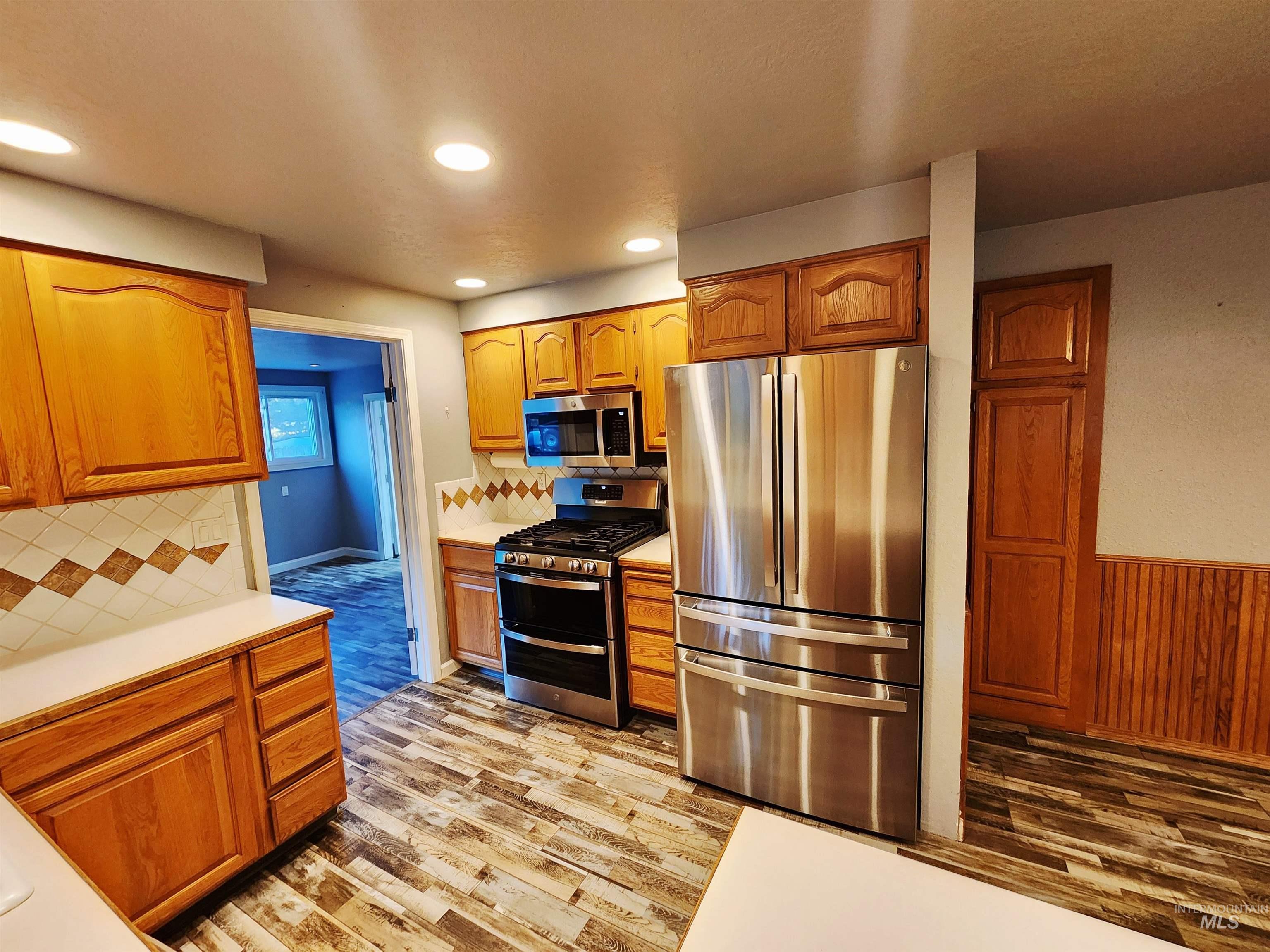 Kitchen with light countertops, stainless steel appliances, brown cabinetry, backsplash, and recessed lighting
