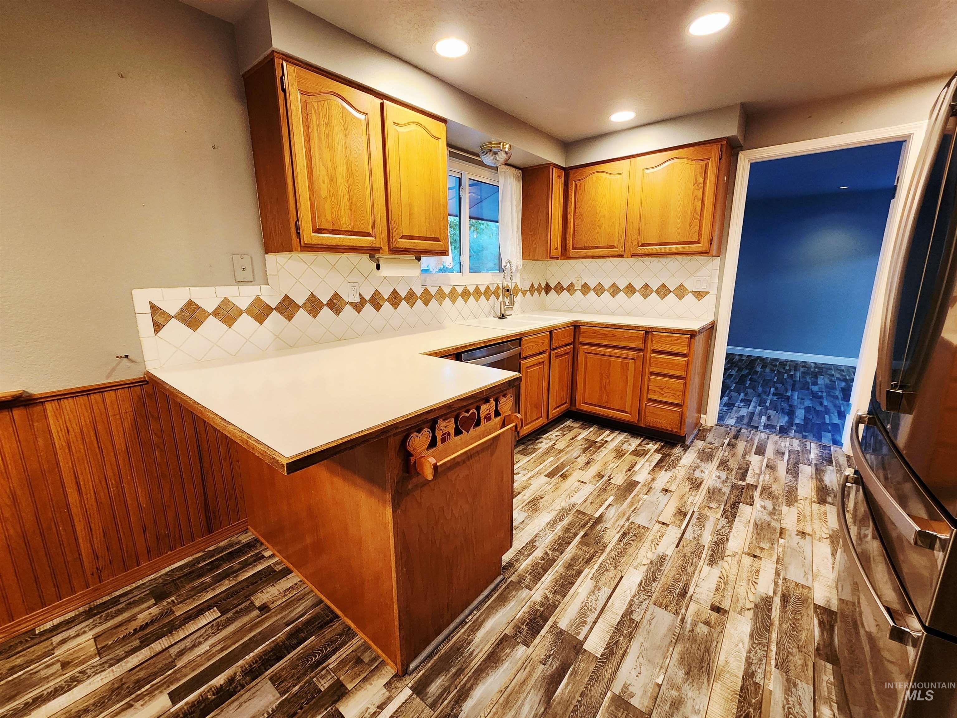 Kitchen featuring brown cabinets, light countertops, backsplash, appliances with stainless steel finishes, and a peninsula
