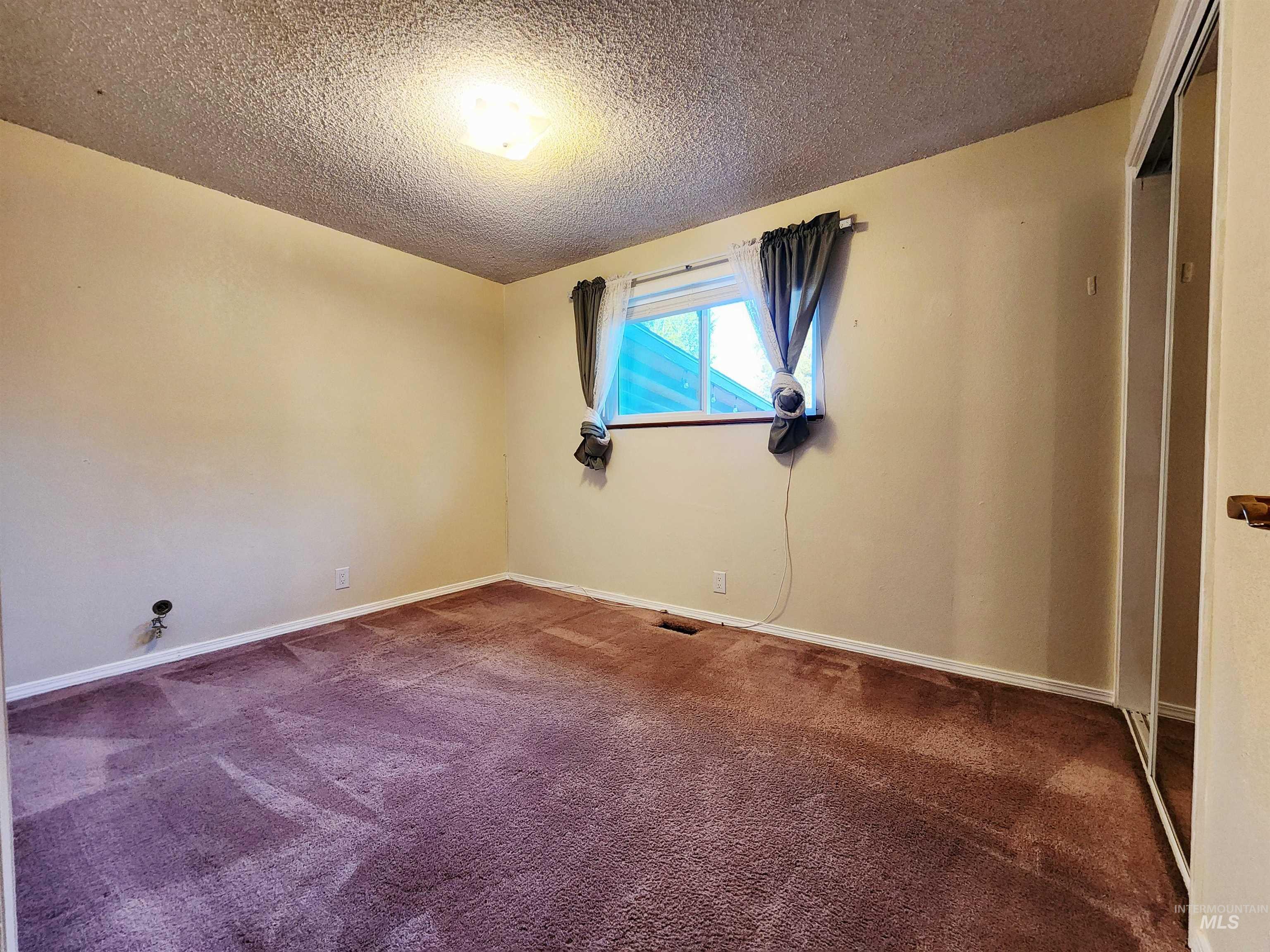 Carpeted empty room with a textured ceiling and baseboards