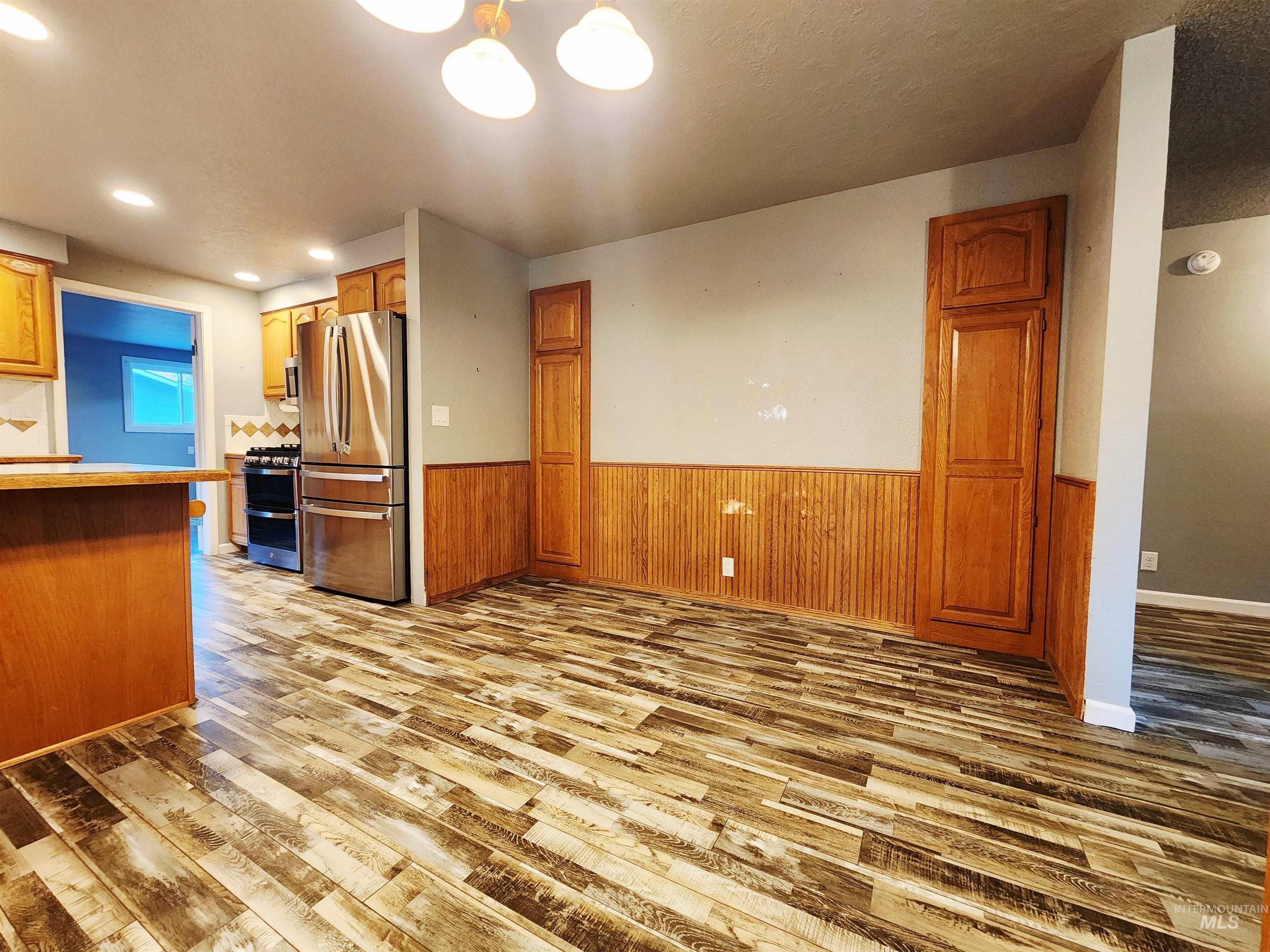 Kitchen featuring a wainscoted wall, appliances with stainless steel finishes, brown cabinets, light wood-style flooring, and wood walls