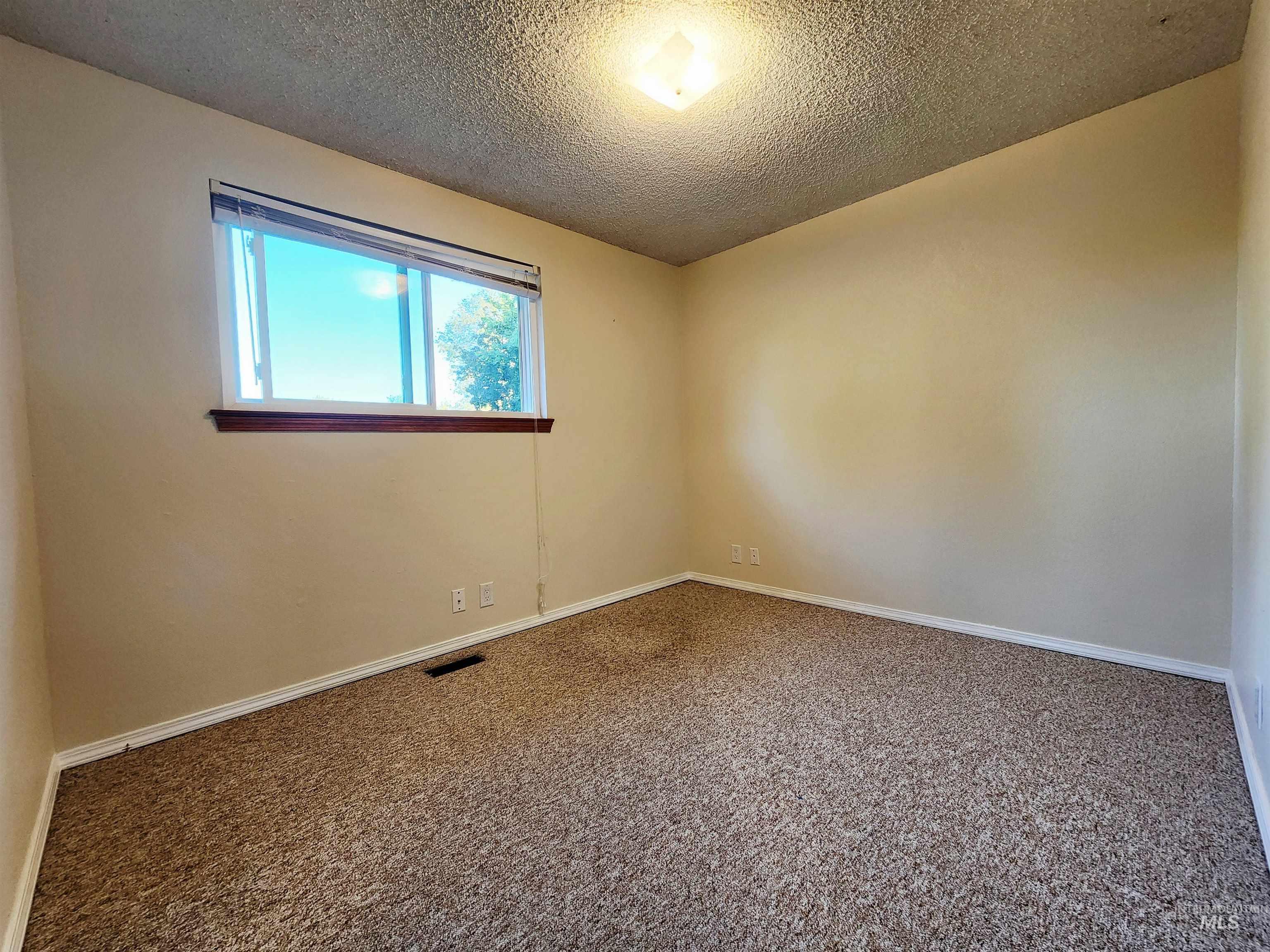 Carpeted spare room featuring a textured ceiling and baseboards