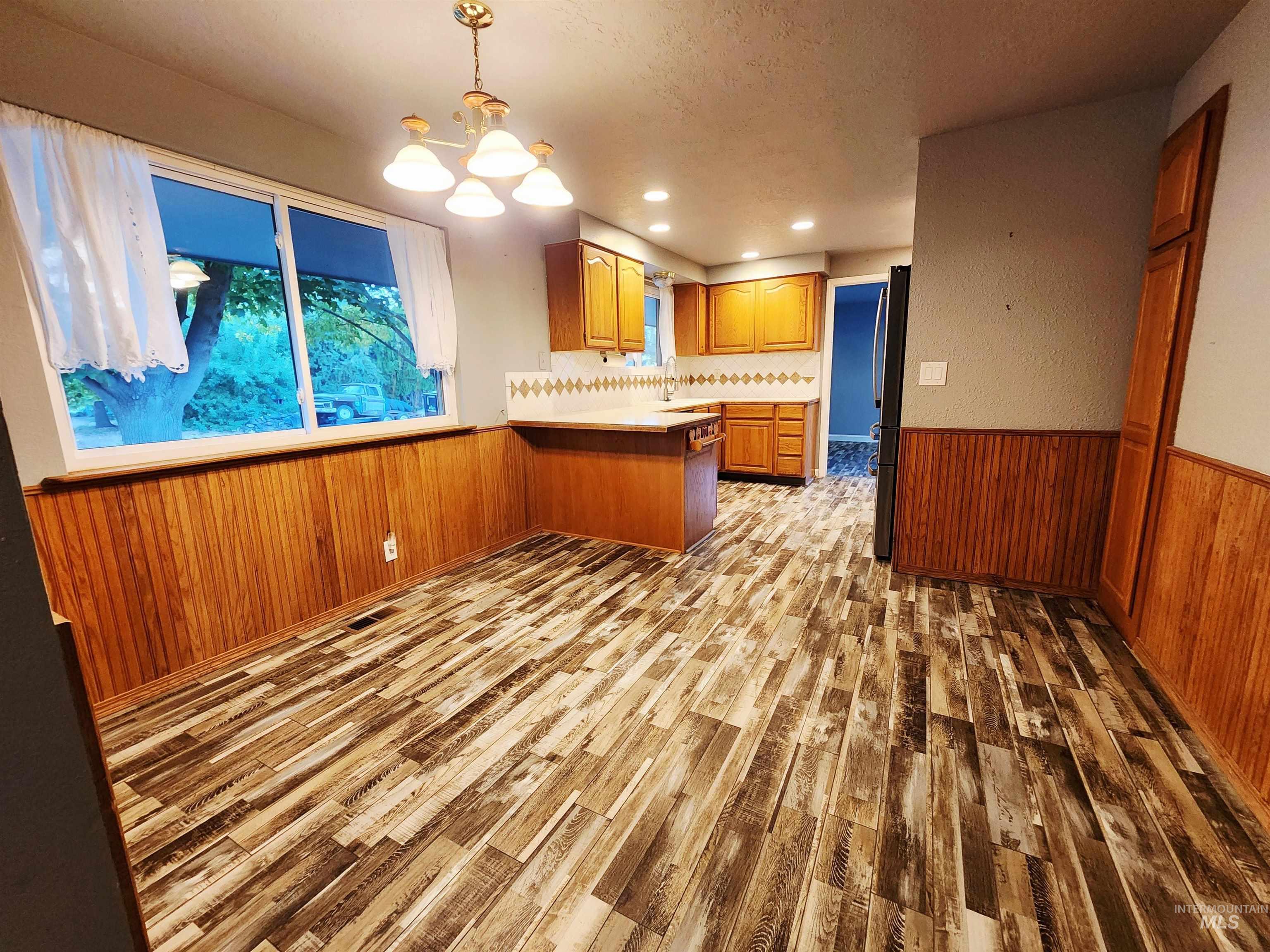 Kitchen featuring wooden walls, a peninsula, a wainscoted wall, hanging light fixtures, and light countertops