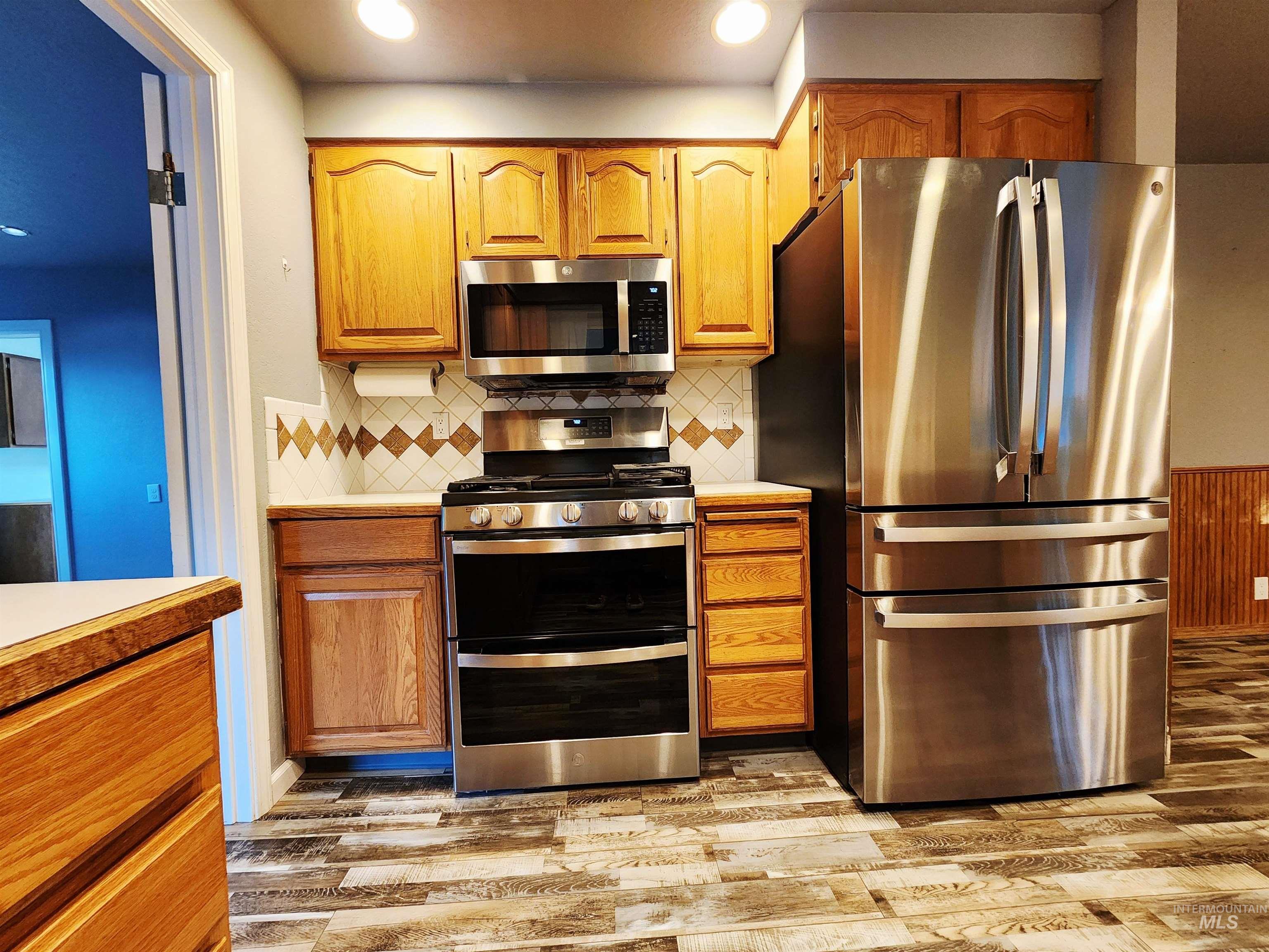 Kitchen featuring stainless steel appliances, brown cabinetry, light countertops, light wood-style flooring, and decorative backsplash