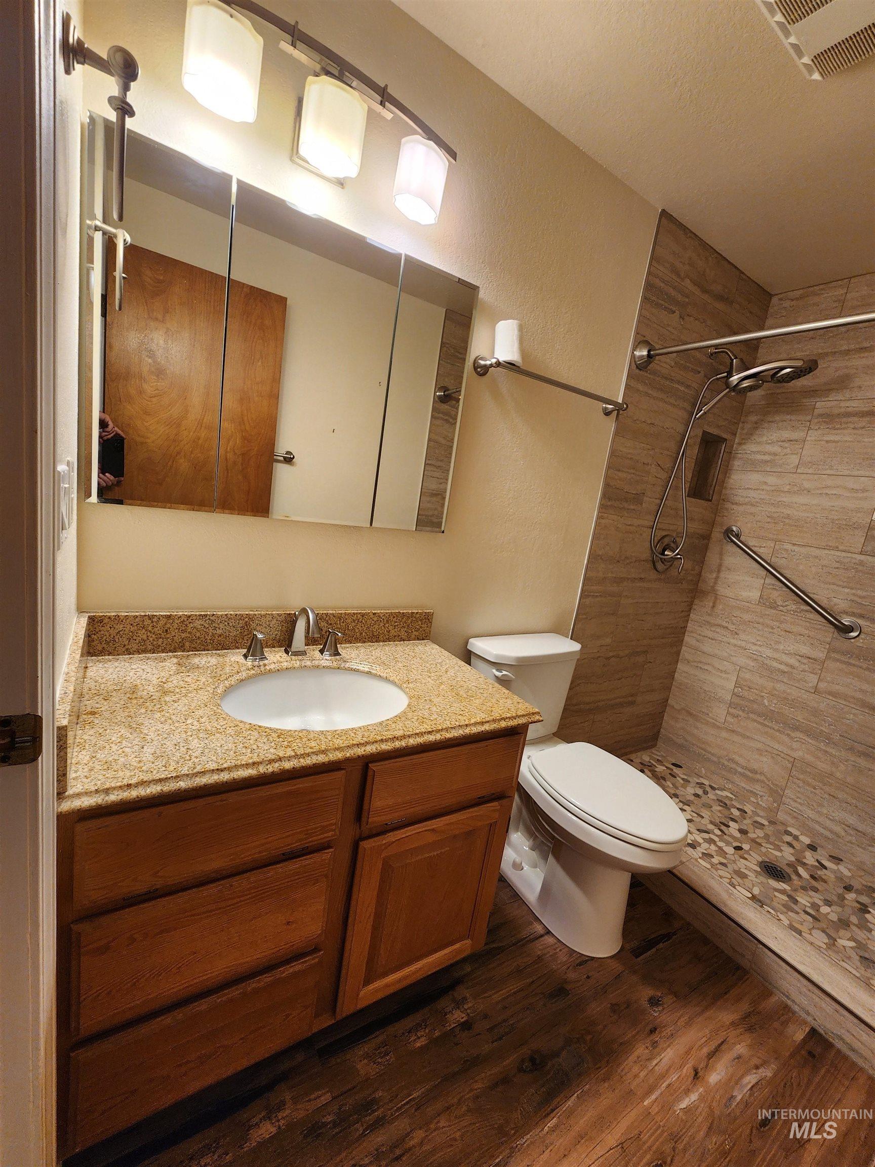 Bathroom featuring vanity, tiled shower, dark wood-style floors, and a textured wall