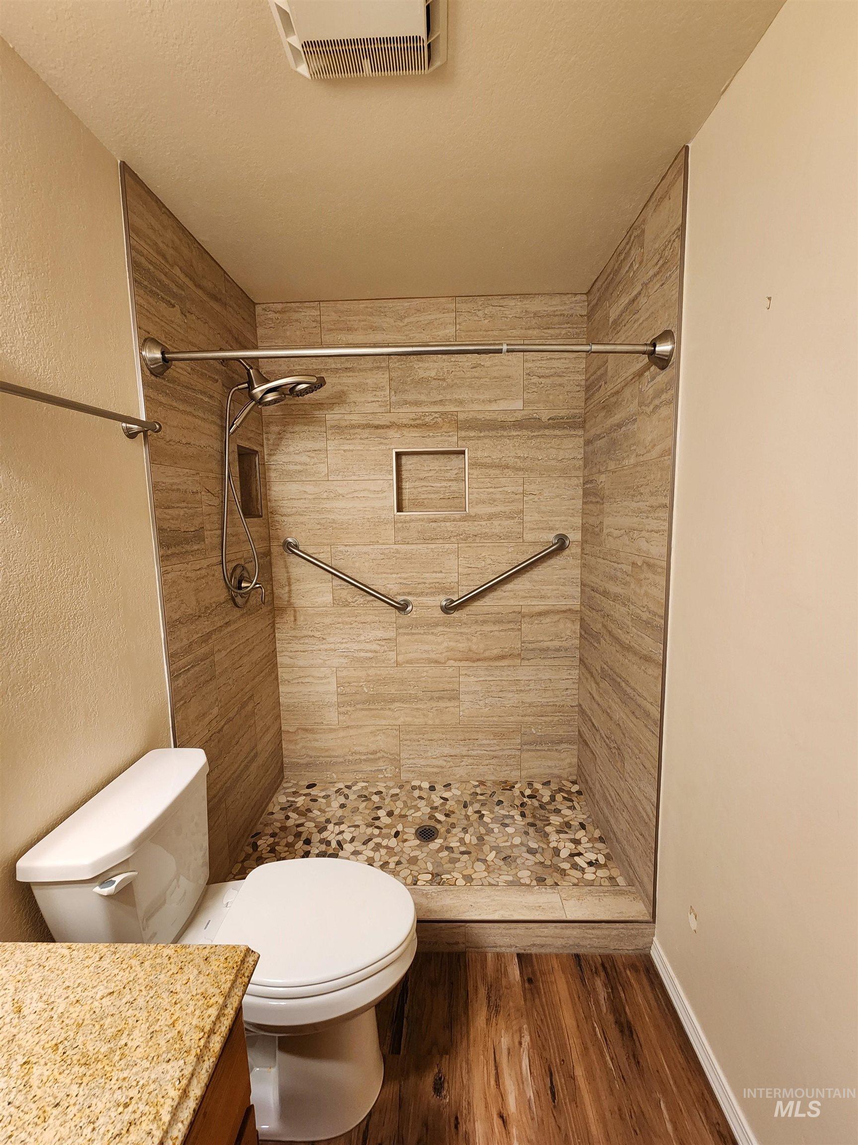Full bathroom with a shower stall, dark wood finished floors, vanity, and a textured wall