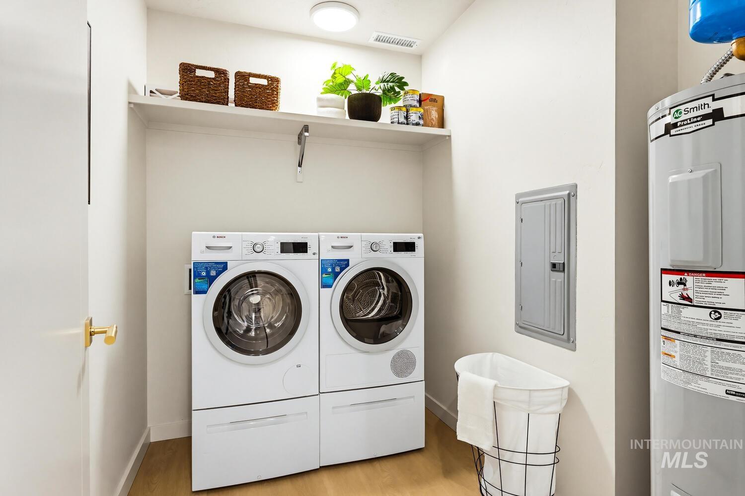 Laundry area featuring electric panel, electric water heater, light wood-type flooring, and washing machine and dryer