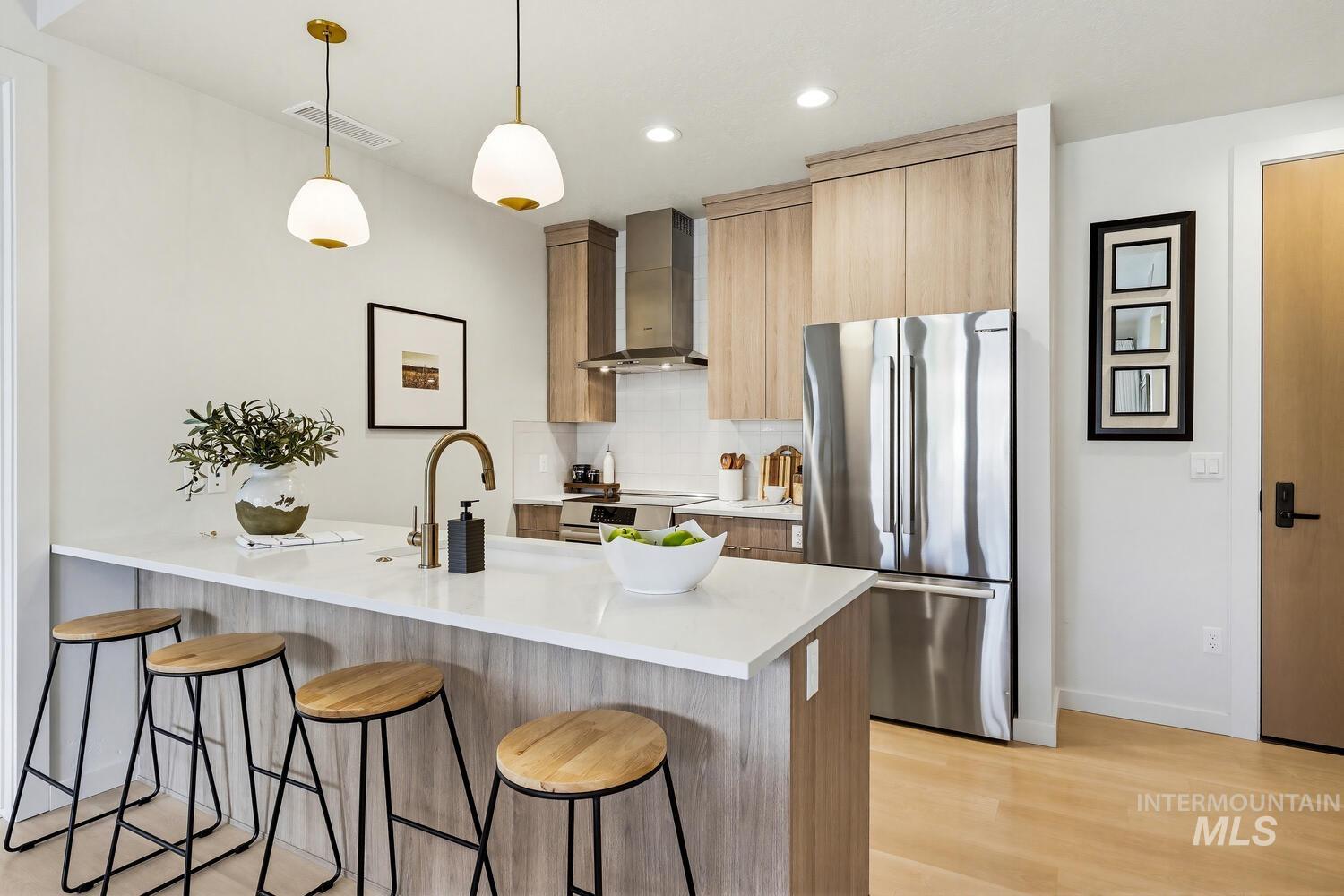 Kitchen featuring a kitchen bar, a peninsula, stainless steel appliances, modern cabinets, and decorative light fixtures