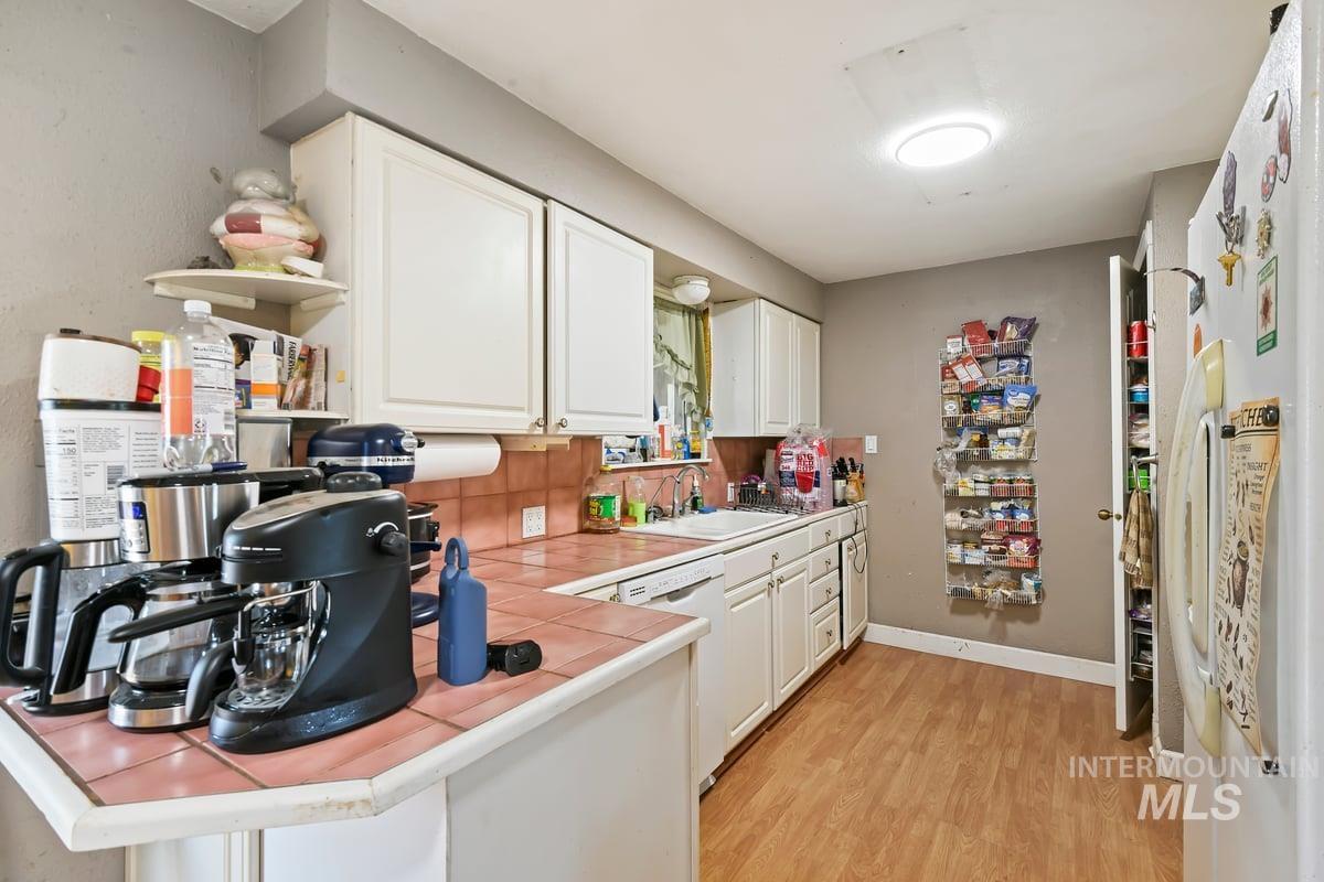 Kitchen featuring tile countertops, white cabinets, light wood-style floors, white appliances, and a peninsula